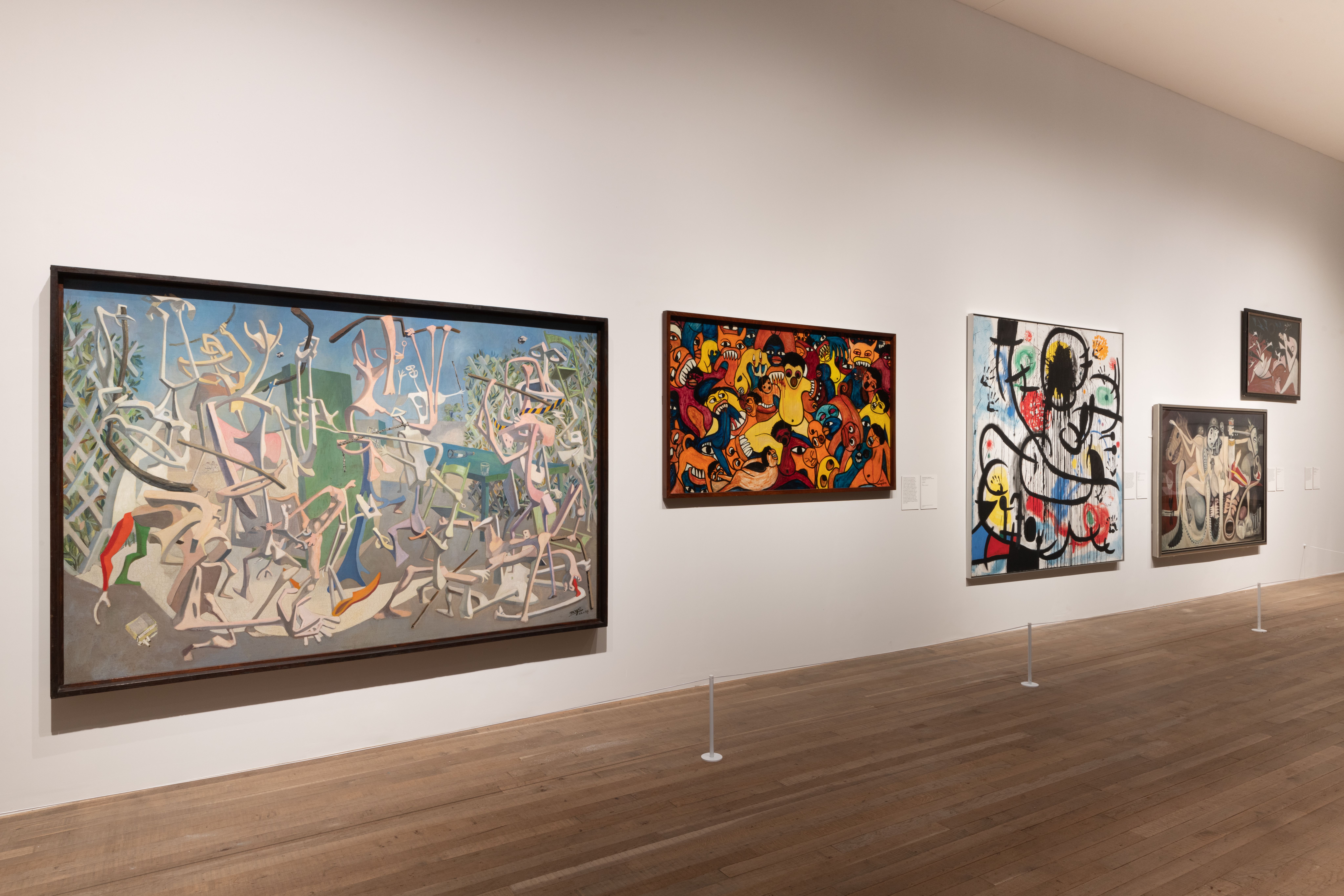 A variety of abstract art paintings in frames hung on the gallery wall, with a view of the wooden floor beneath.