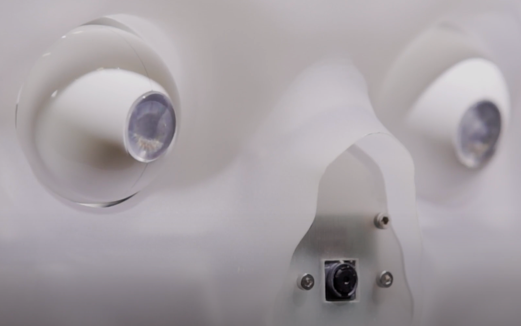 A section of a white mechanical device, featuring two circular lenses positioned side-by-side and a black button in the mi...