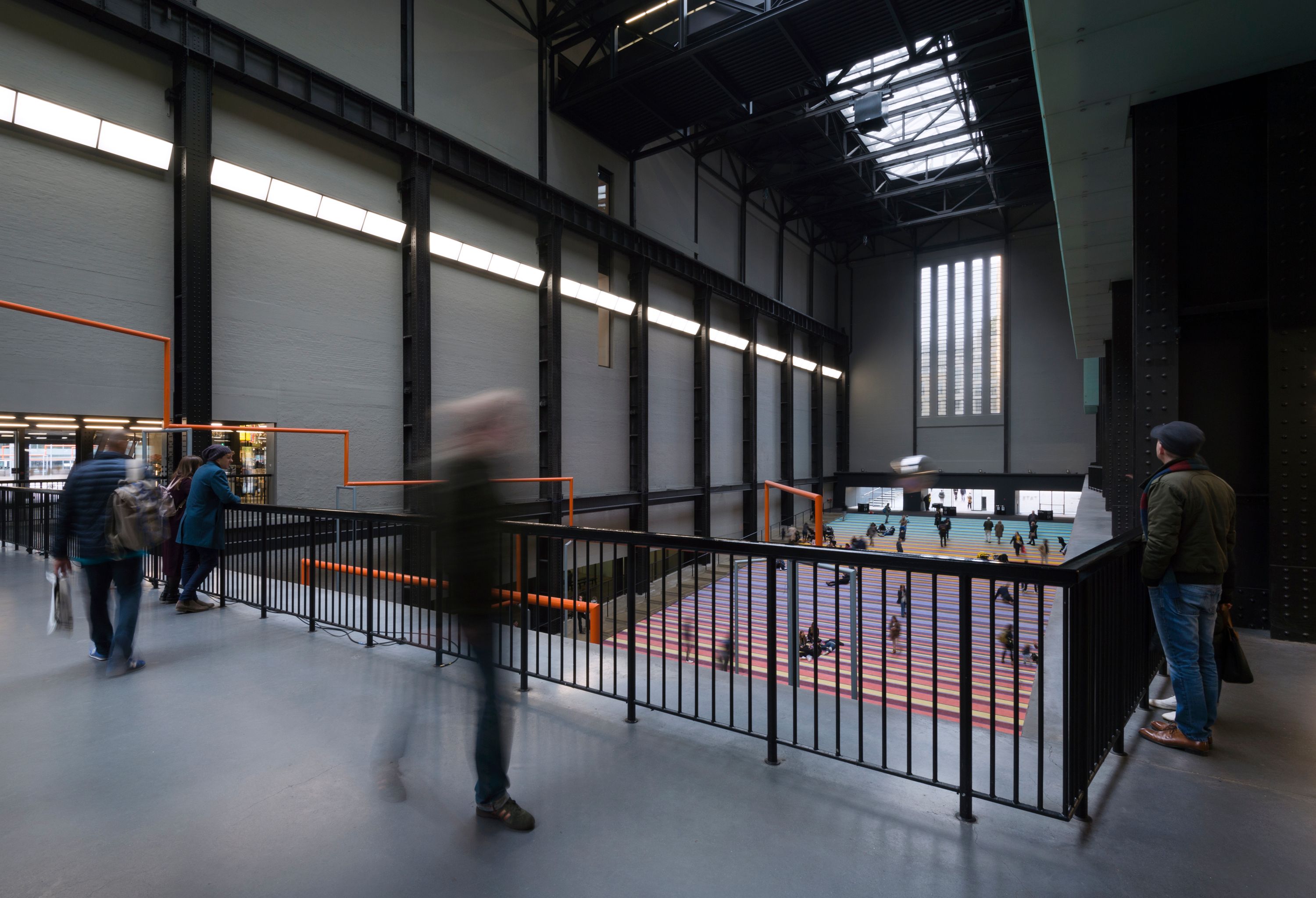 A time-lapse photograph capturing the motion blur of numerous individuals moving in a spacious art gallery.