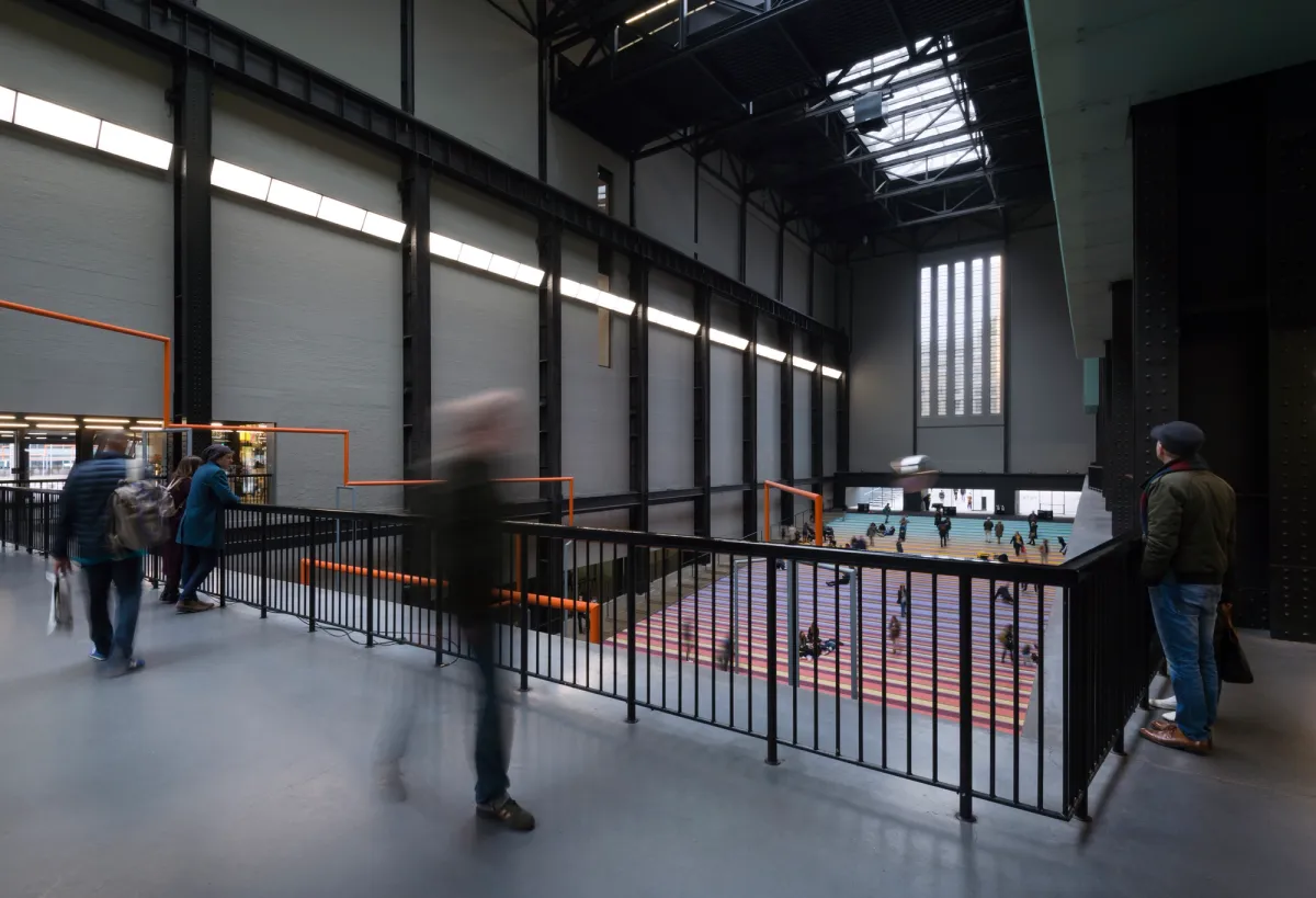 A time-lapse photograph capturing the motion blur of numerous individuals moving in a spacious art gallery.