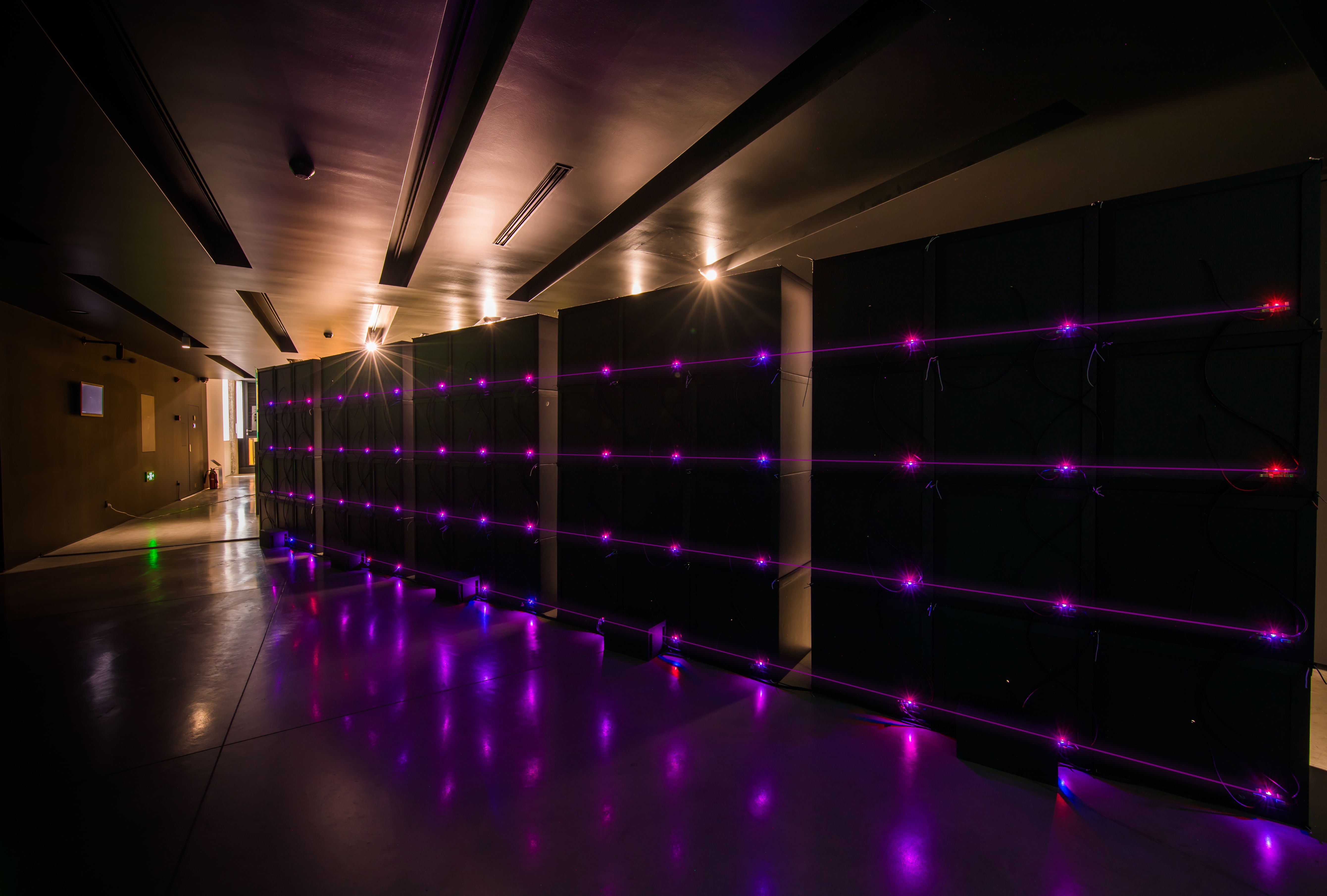 Dark room with wall of black boxes and glowing purple lights.