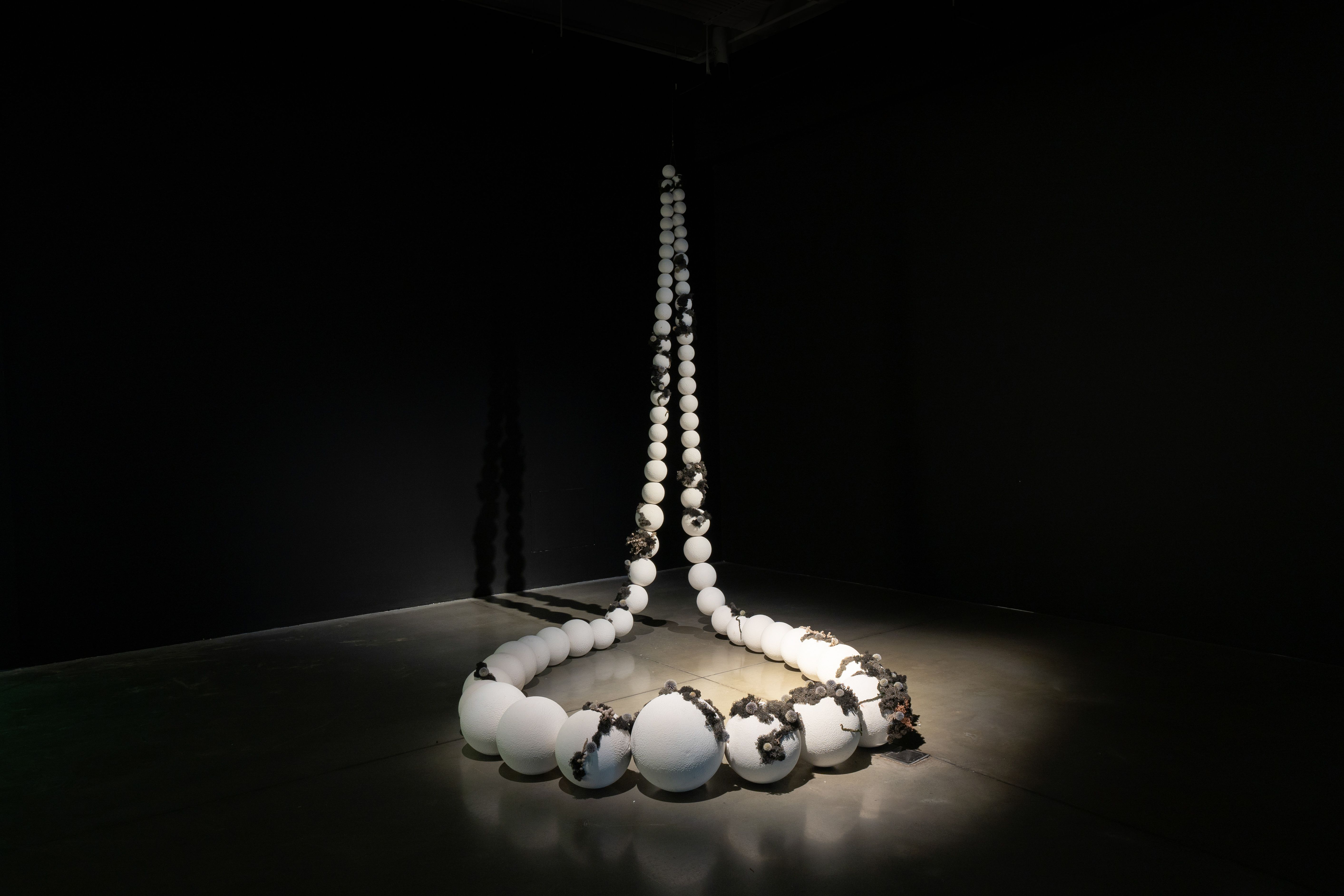 A sculpture of a life-sized beaded necklace partially covered by moss.
