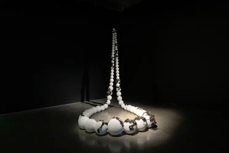 A sculpture of a life-sized beaded necklace partially covered by moss.