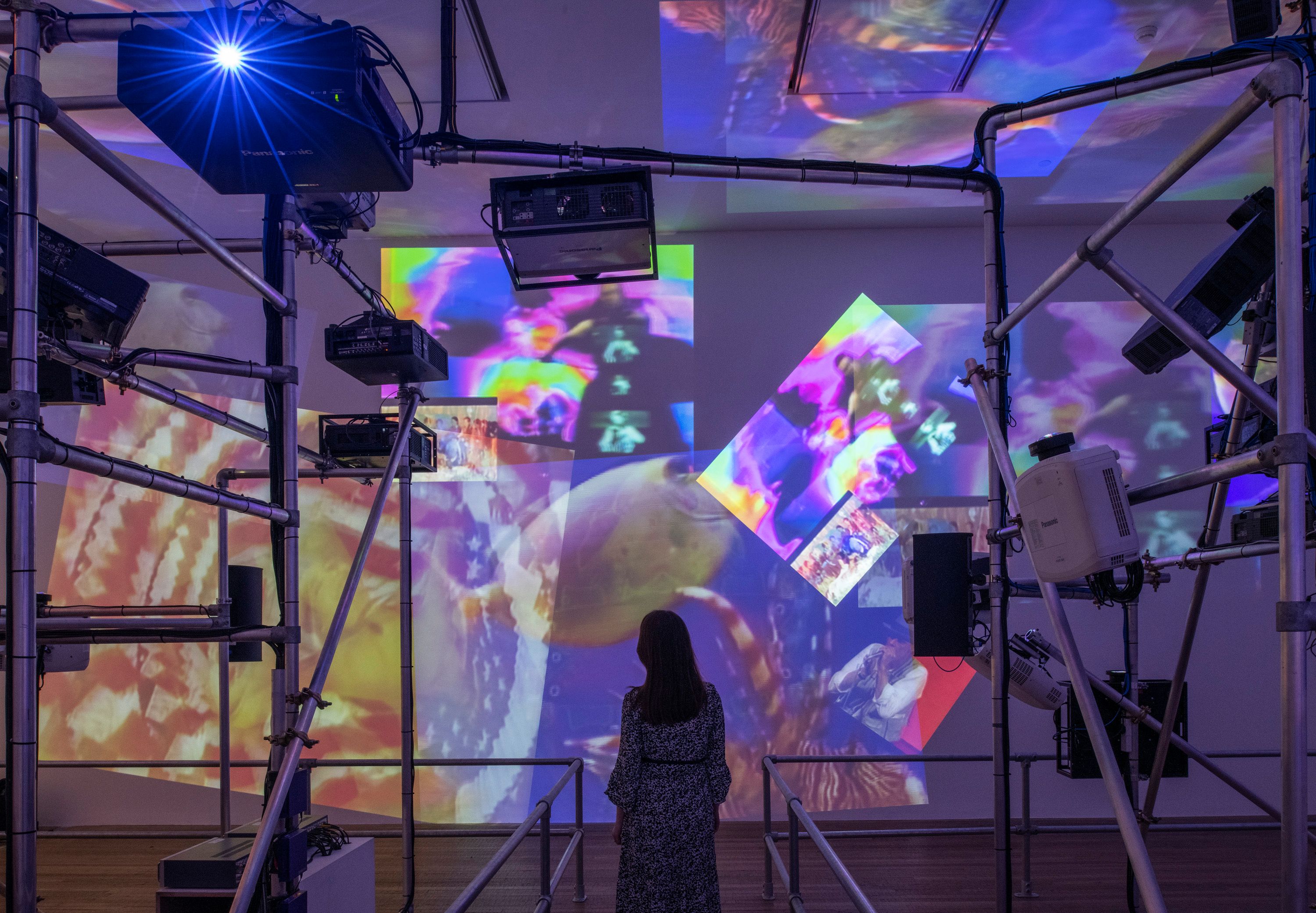 A person in a gallery examining a wall featuring a series of projected photos showcasing the Sistine Chapel as it appeared...