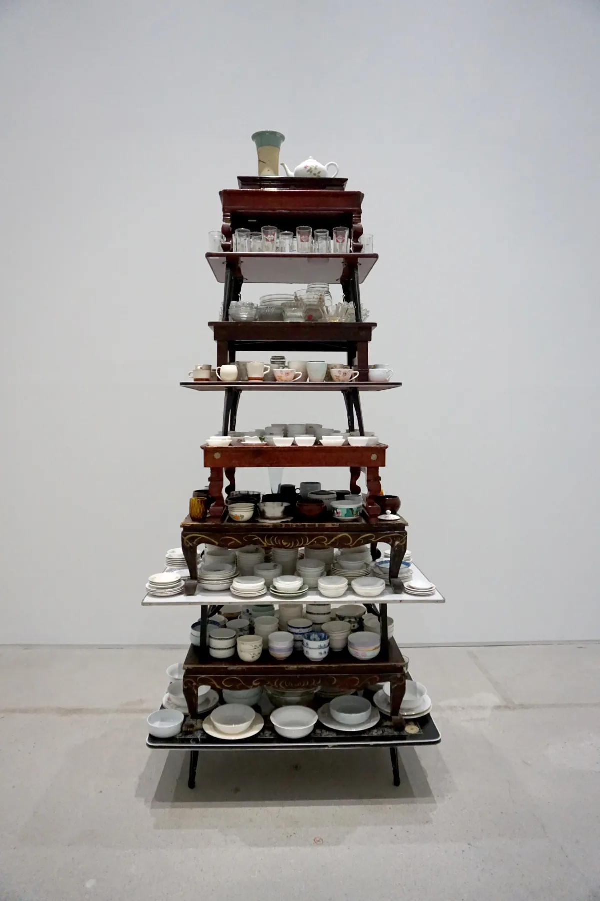 A unique piece of furniture constructed from tables stacked on each other, adorned with numerous stacked cups and saucers.