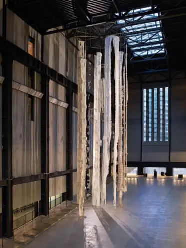 An enormous windchime installation fills a hall, adorned with long, tattered white materials.