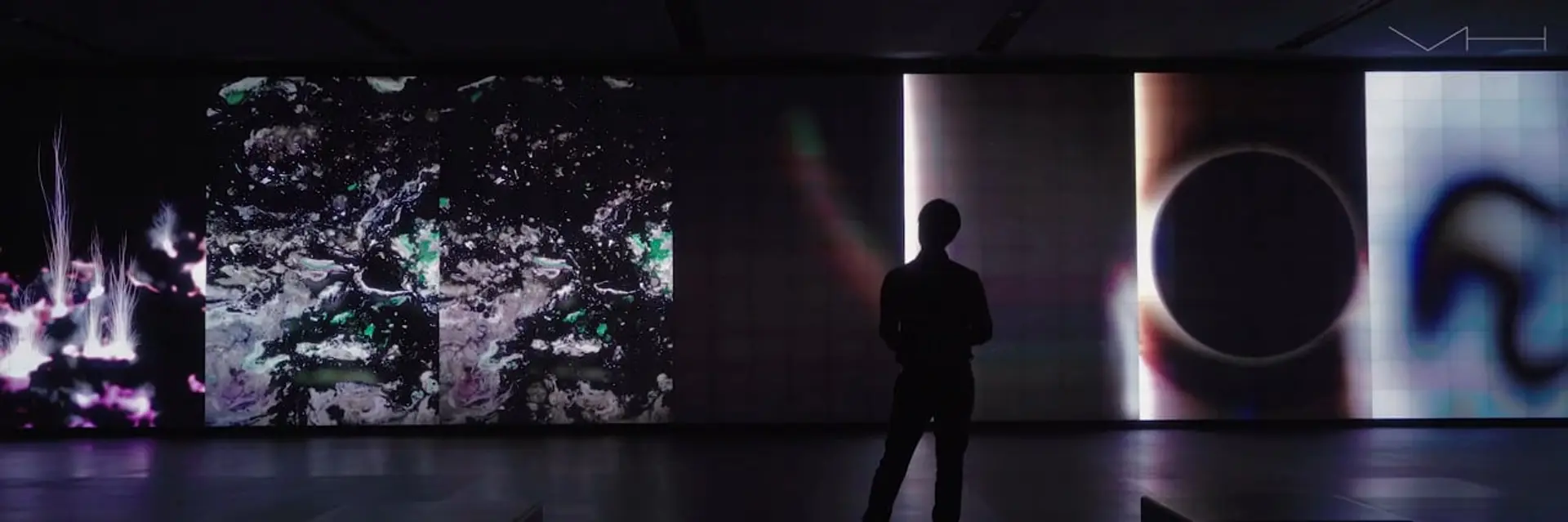 Silhouetted figure stands observing large, vivid digital art displays on gallery walls.