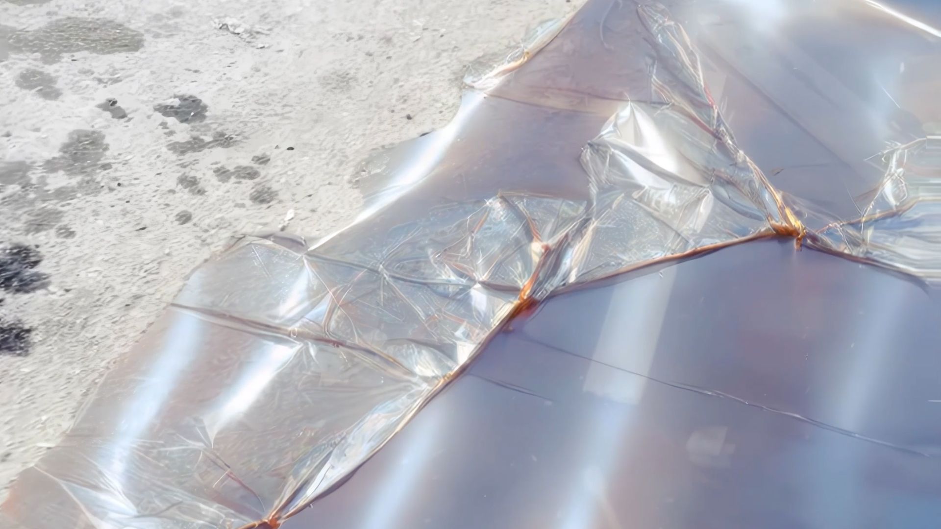 A silvery puddle spread across a rough concrete surface, reflecting dim light.