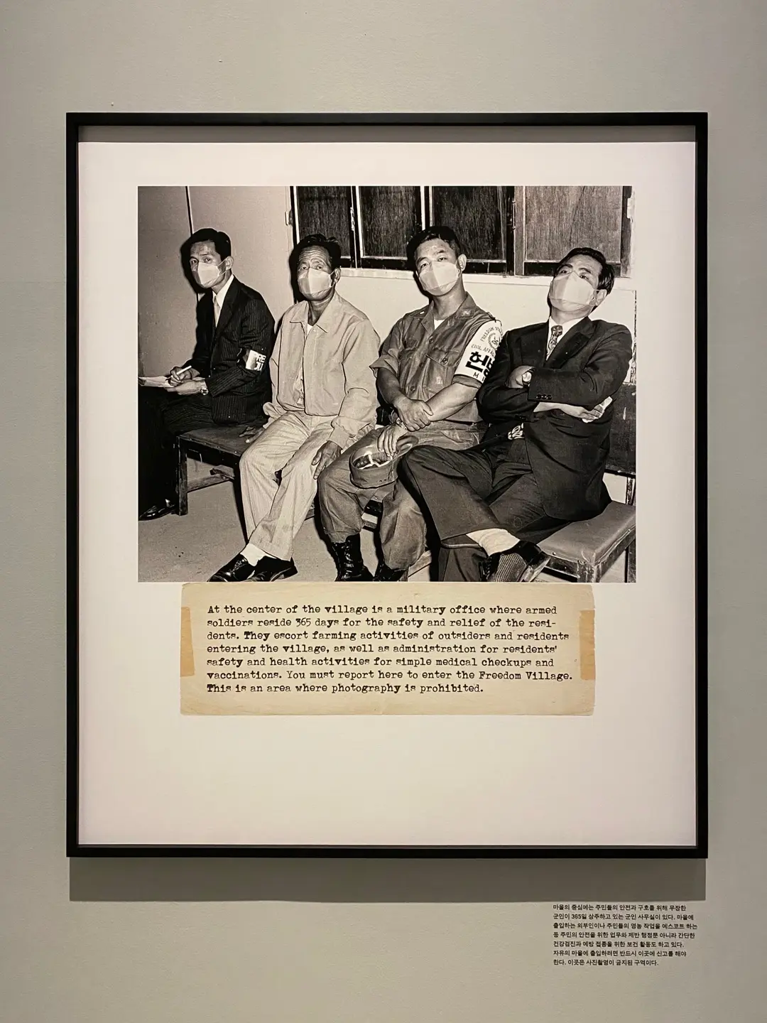 A framed digital print measuring 120x140cm is mounted on a wall, depicting four individuals with an accompanying caption about Freedom Village and Influenza.