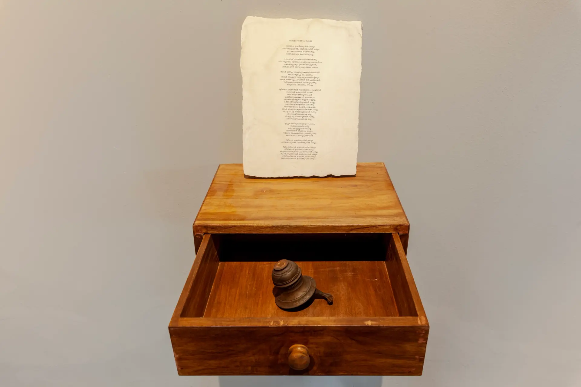 An install image showing a drawer containing a bronze object. A piece of paper stands on top.