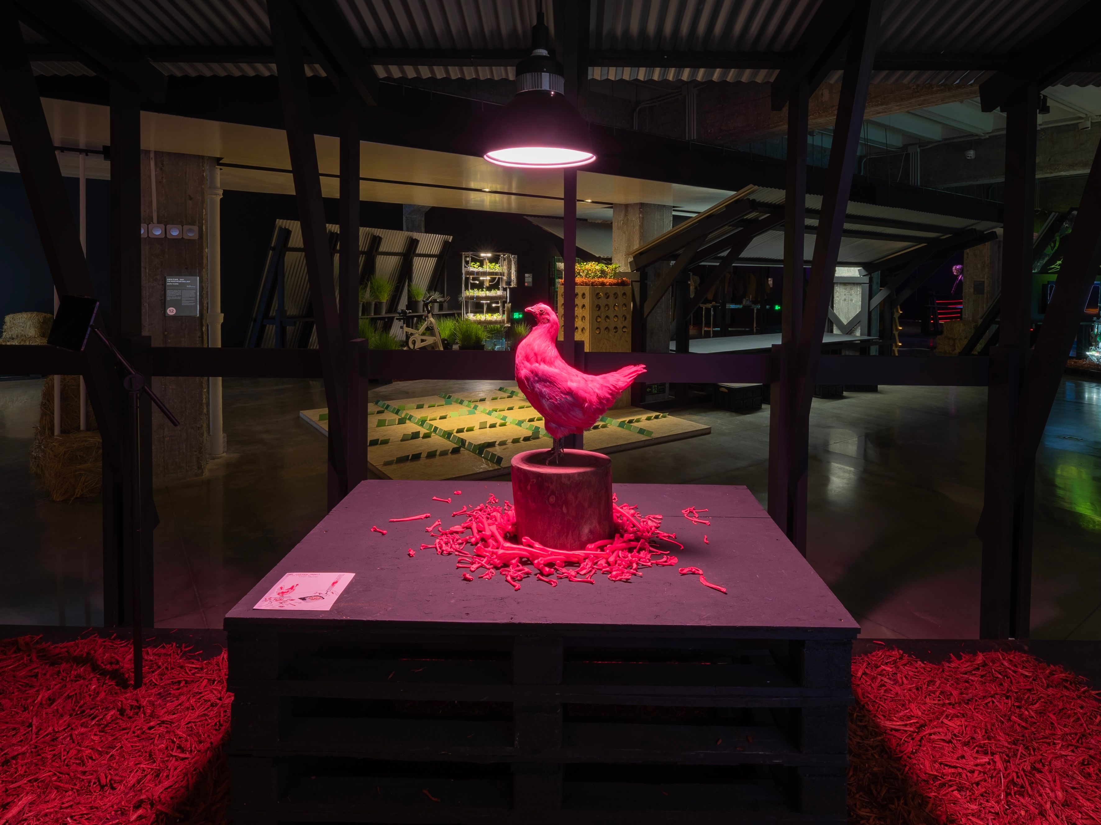 Pink bird sculpture on a pedestal with red shavings, illuminated by an overhead lamp.