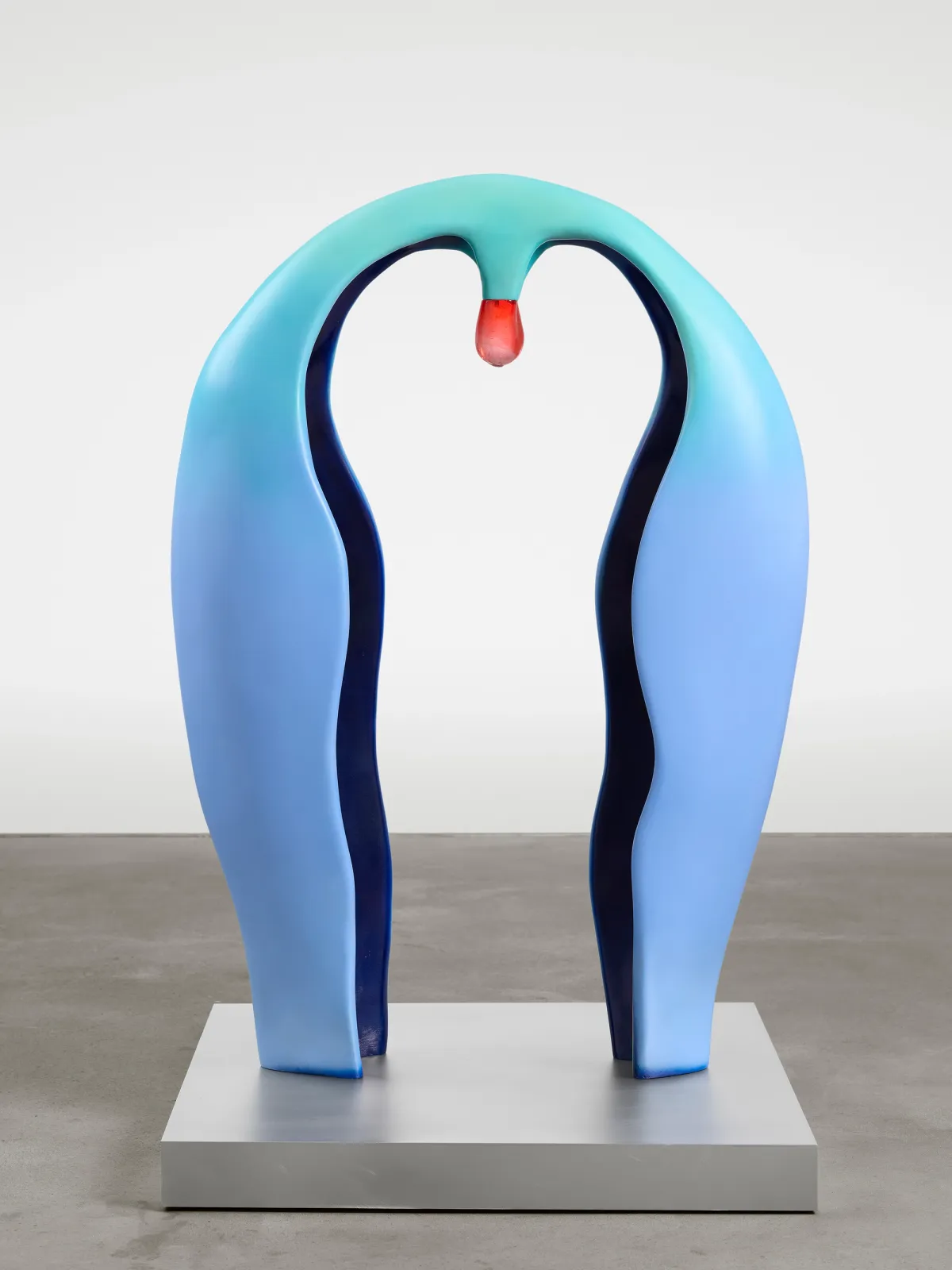 An azure, horseshoe-shaped sculpture with a red drop in the center, made of polymer, steel, and acrylic paint, standing on a raw aluminum and mdf pedestal.