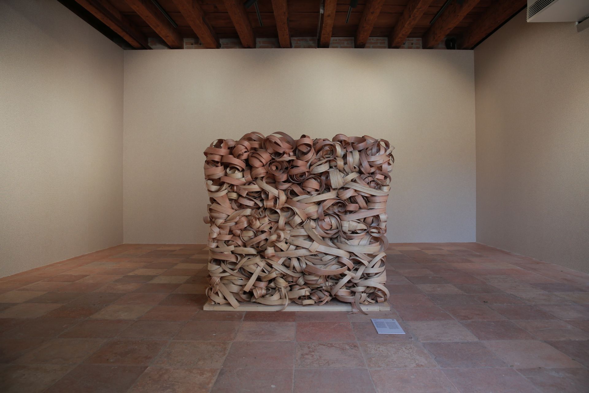 Interior with a cube-shaped art piece of intertwined beams and leather belts on a tiled floor.