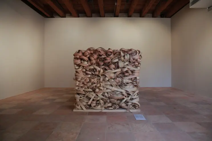 Interior with a cube-shaped art piece of intertwined beams and leather belts on a tiled floor.
