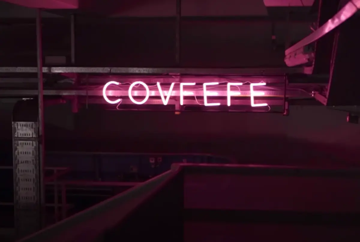 A dark industrial interior lit by the vibrant pink LED light of letters spelling the word "covfefe."