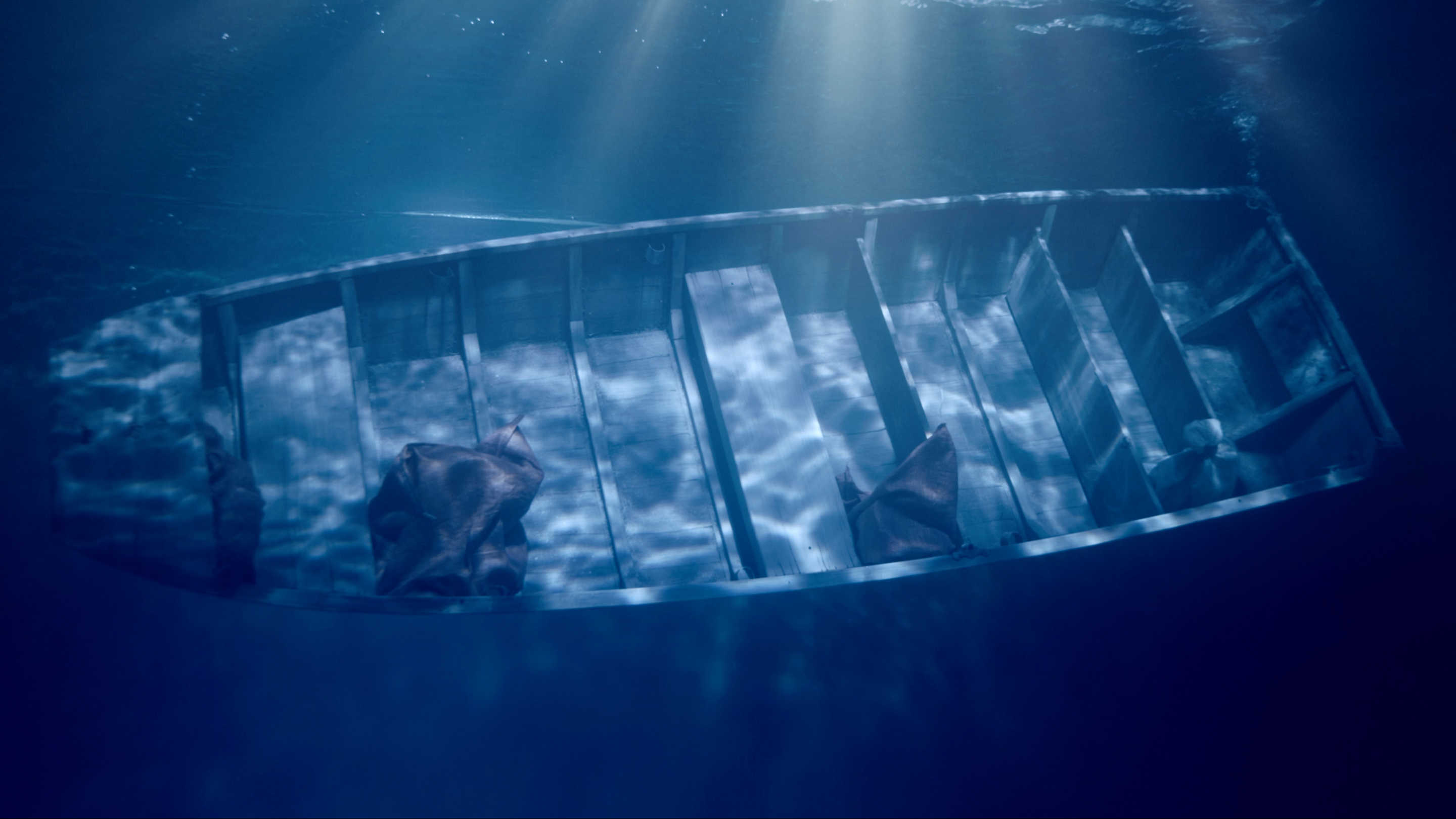 An underwater photograph showing a rowboat sinking to the ocean floor, with sun flares penetrating from above the water su...
