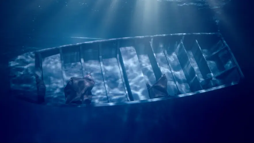An underwater photograph showing a rowboat sinking to the ocean floor, with sun flares penetrating from above the water su...