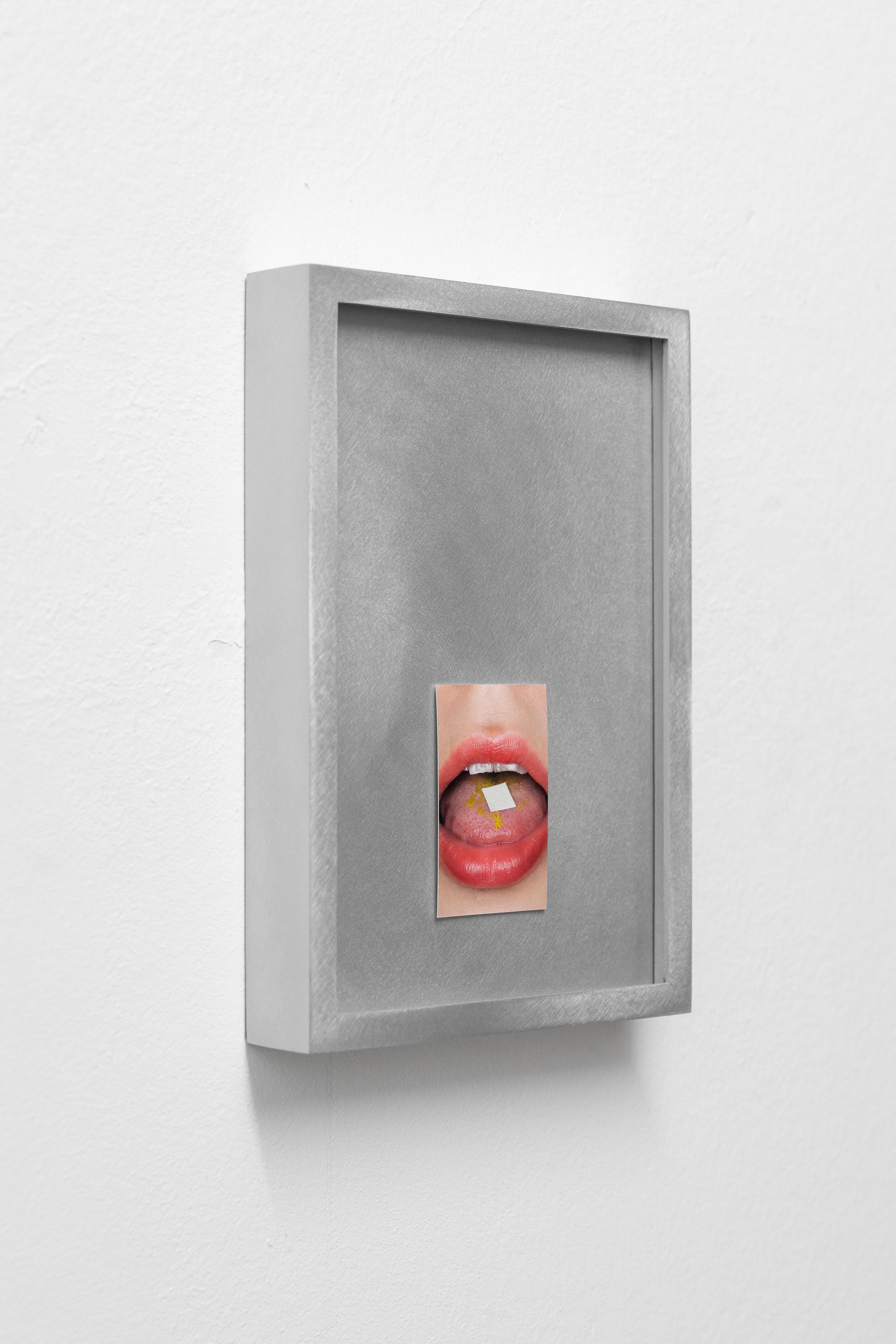 A side-view of a brushed metal frame displaying a small photo of a mouth holding a tab on the tongue.