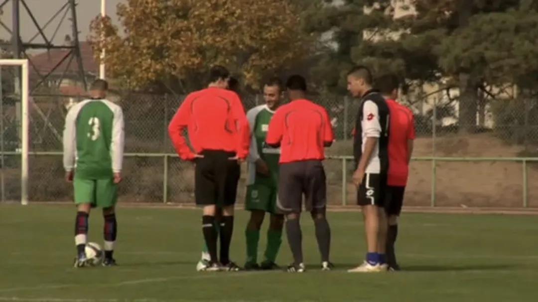 Outdoor scene with soccer players huddled around a referee.