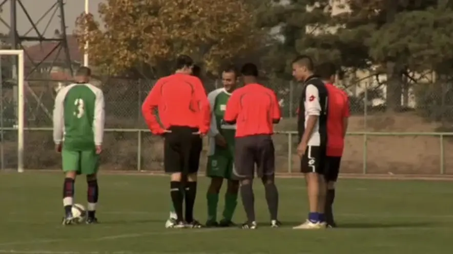 Outdoor scene with soccer players huddled around a referee.