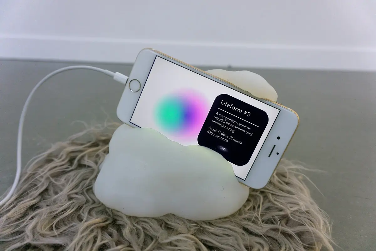 A white iPhone is nestled within a silicone rock-like holder, connected to a USB cable for charging.