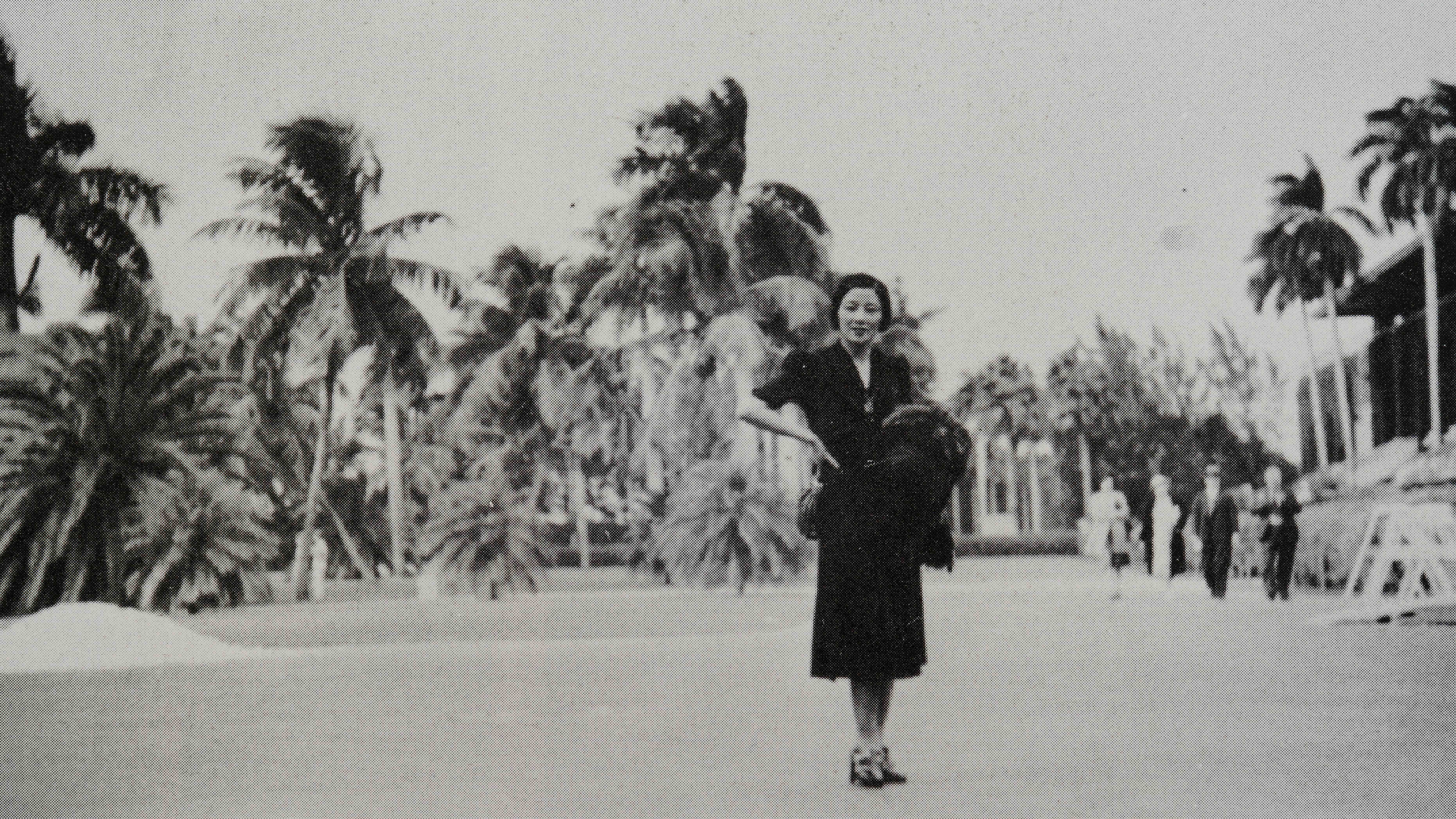 A vintage black and white photograph depicts a person posing in front of towering palm trees.