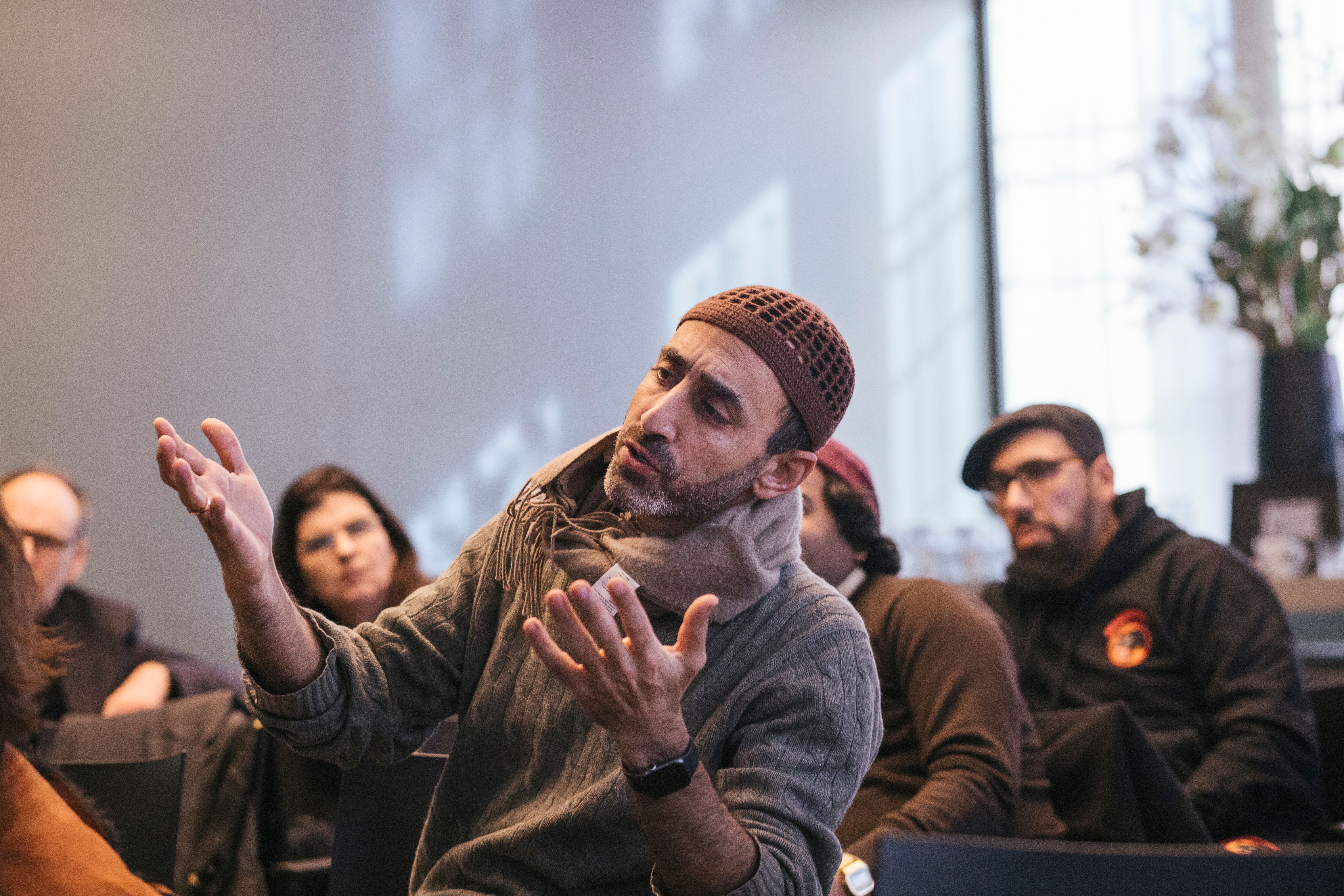 A seated individual in an audience, actively engaged in discussion using hand gestures.