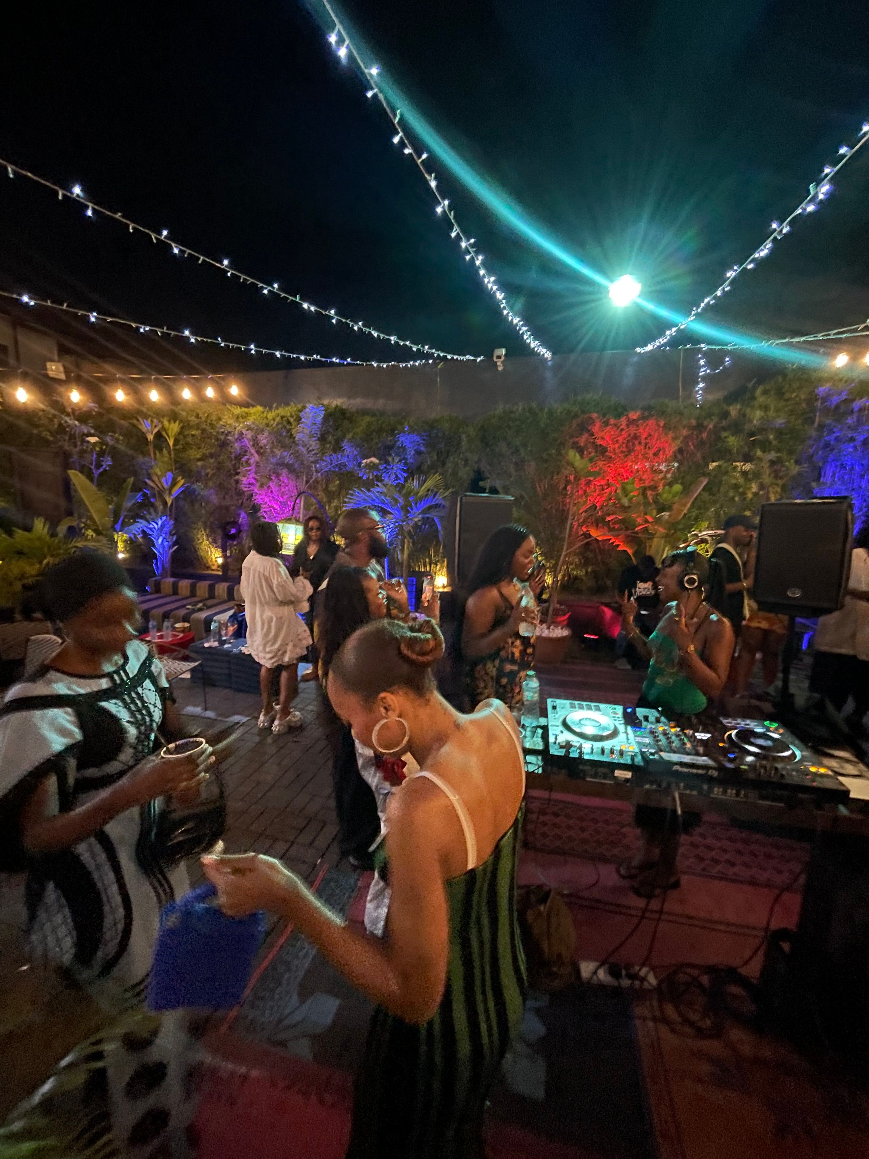 A lively outdoor night gathering with dancing and colorful lighting.