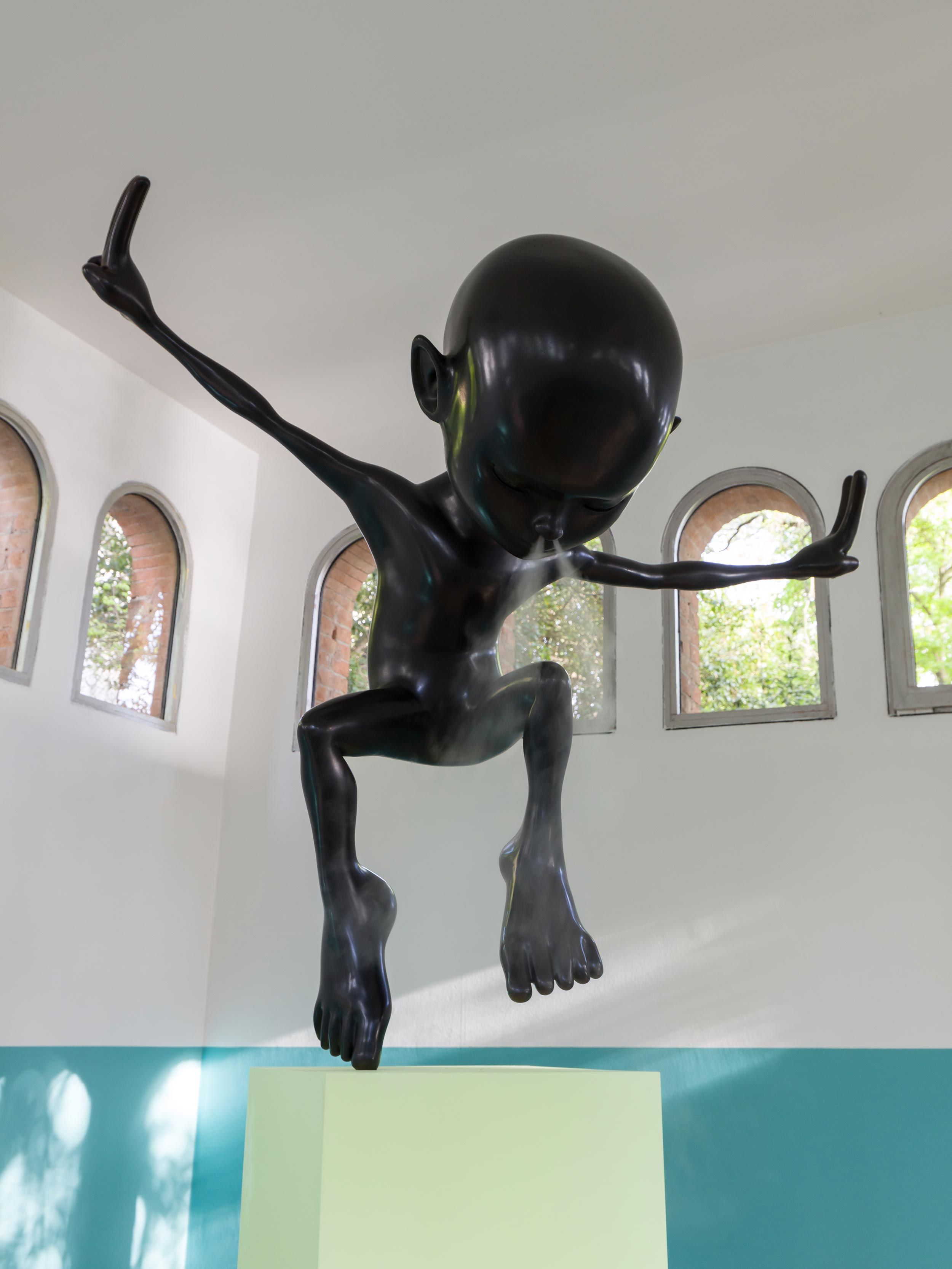 Close-up of a shiny black humanoid sculpture with extended limbs on a green pedestal, set against a white and teal two-ton...