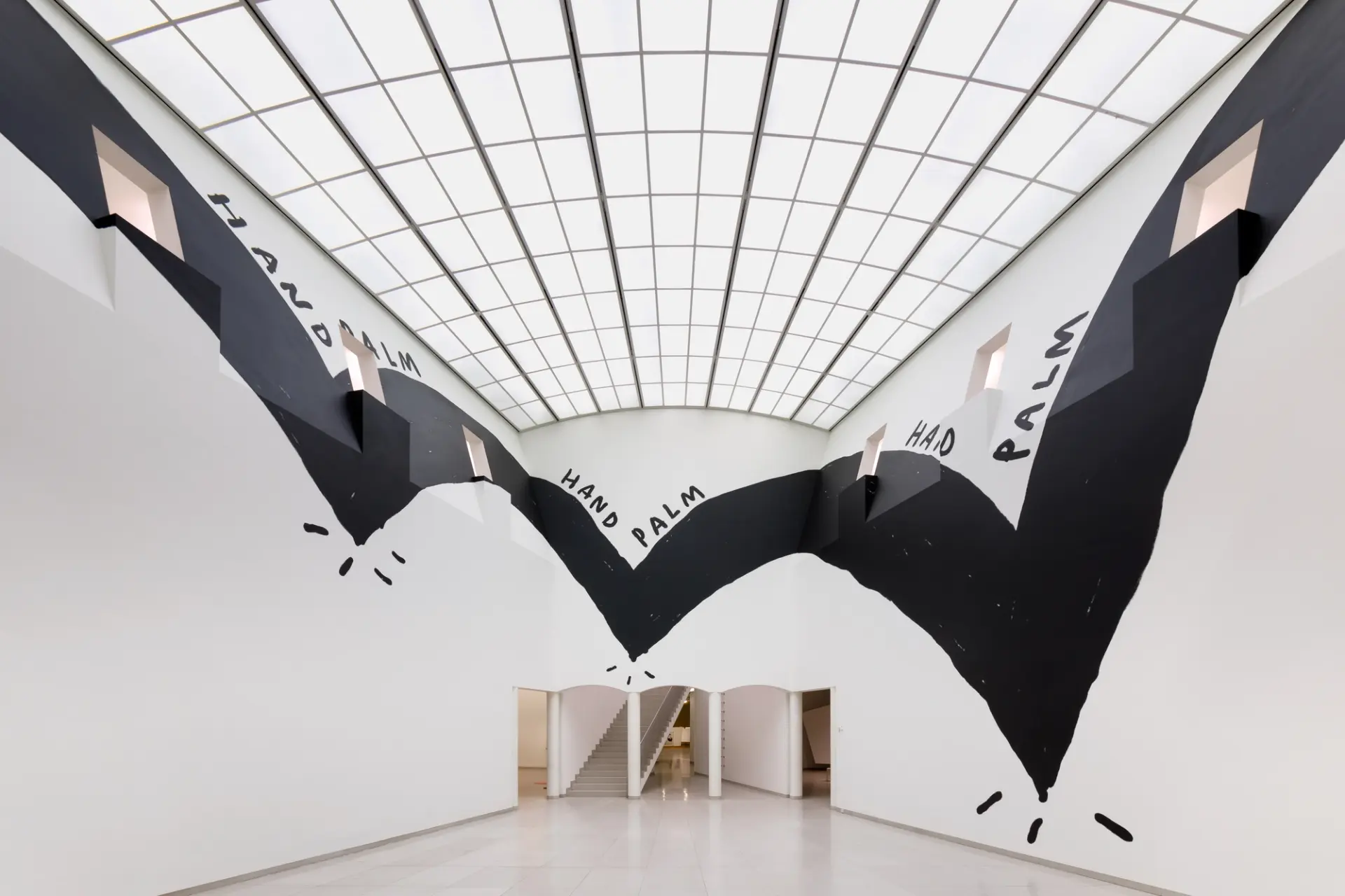 A large-scale wall mural inside a gallery with bold black shapes and the words “HAND PALM HAD PALM”.