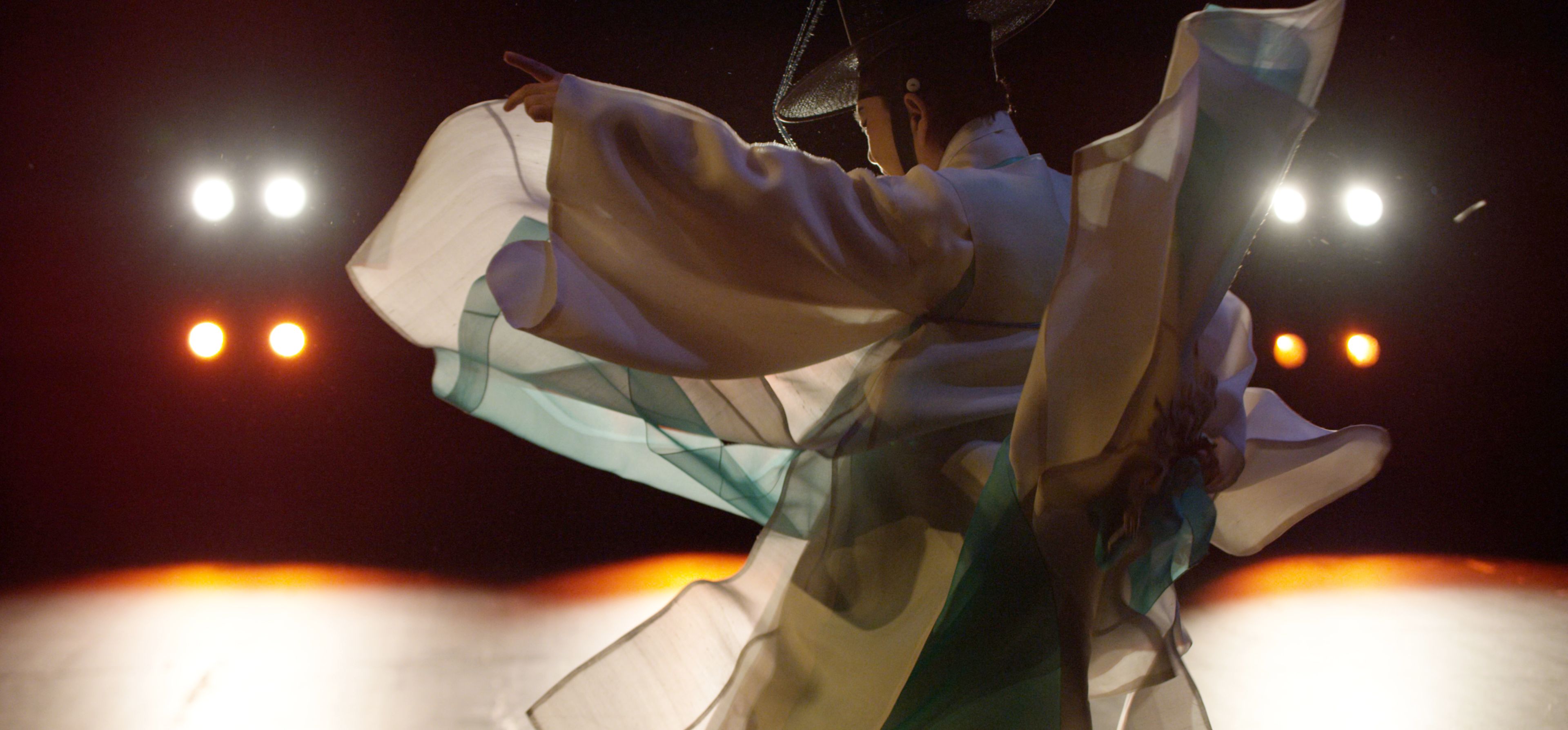 A costumed performer illuminated under multiple spotlights in an audiovisual installation featuring multi-channel video an...