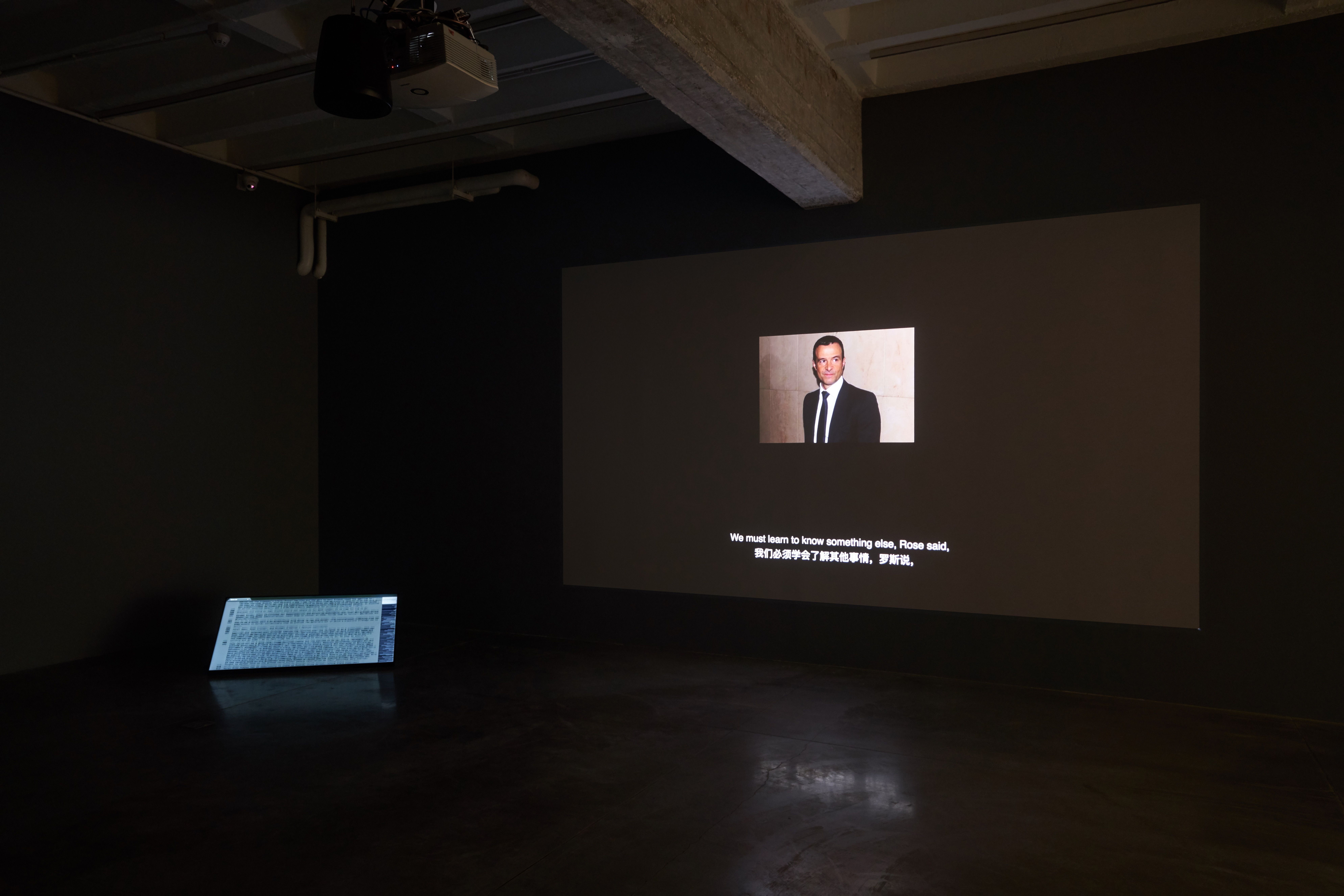 Dark room with projector displaying a man's image and text.