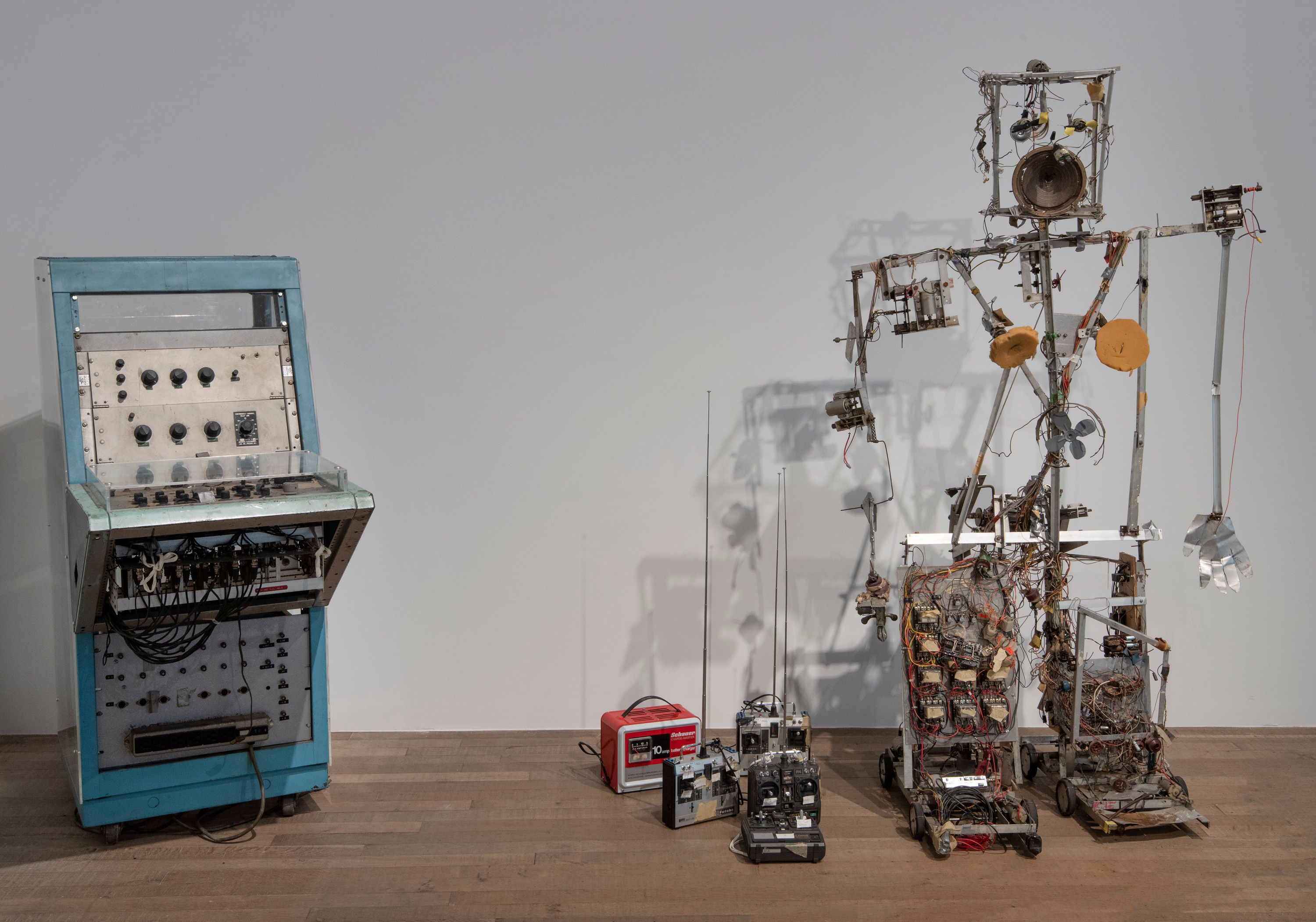 An installation featuring various electronic machines: a console with knobs and wires on the left, a robot composed of ele...