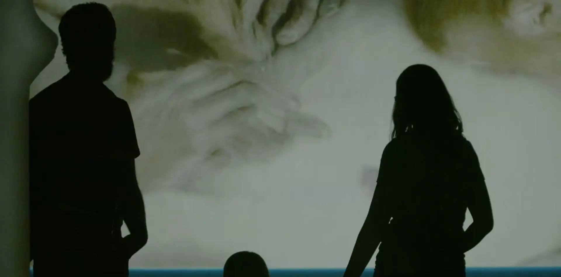 Silhouettes of two people viewing a large projection of an abstract painting.