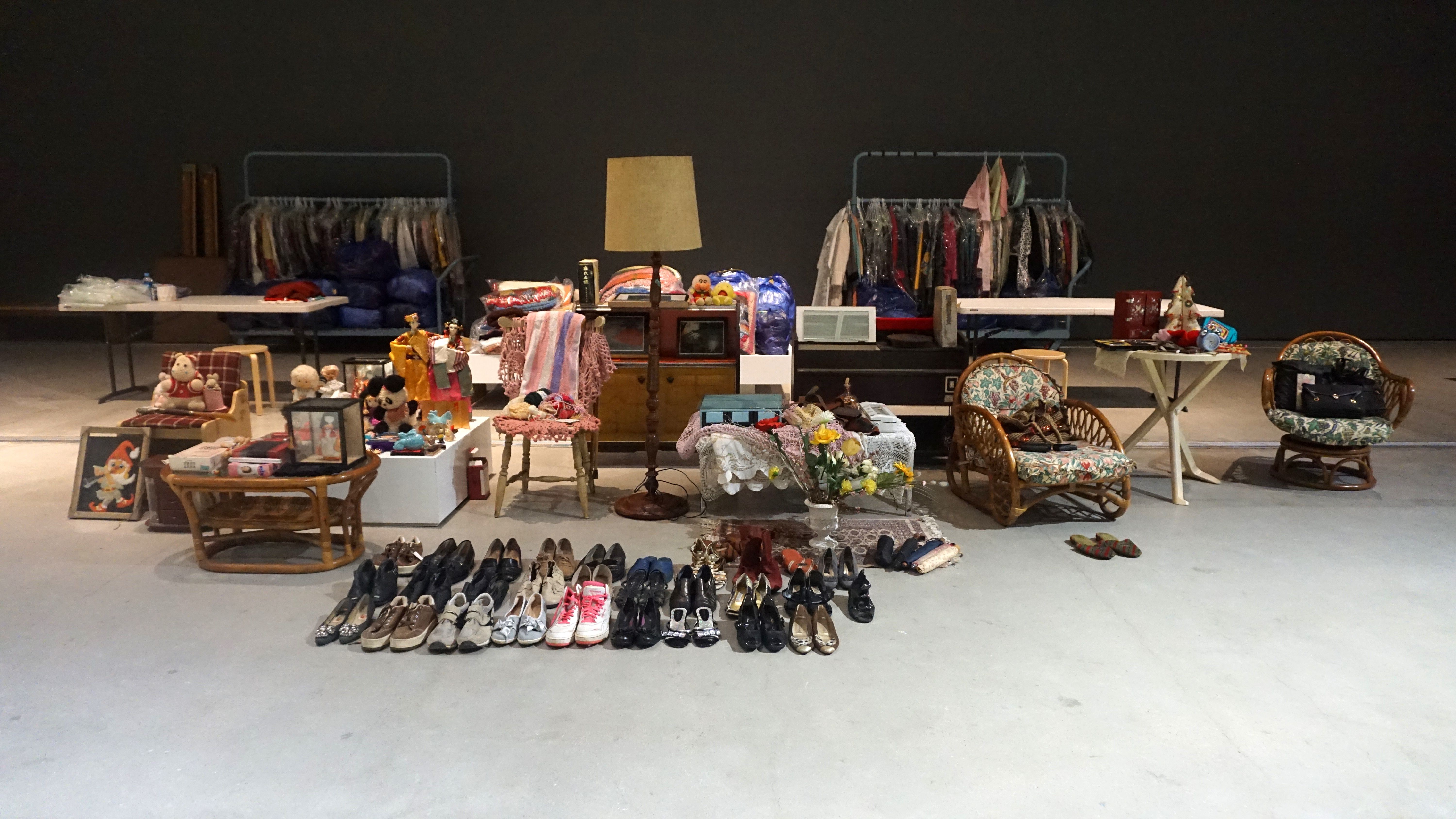 A room with white floors and black walls filled with an assortment of items laid out for a yard sale. Various objects incl...