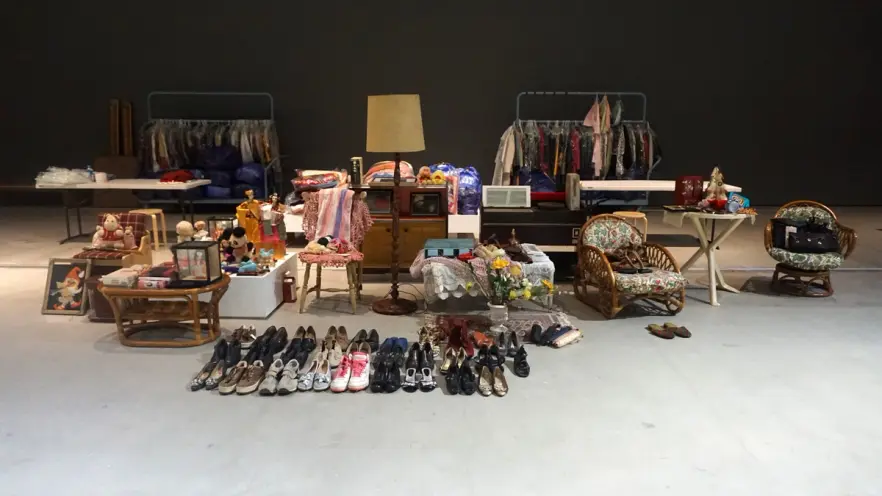 A room with white floors and black walls filled with an assortment of items laid out for a yard sale. Various objects incl...