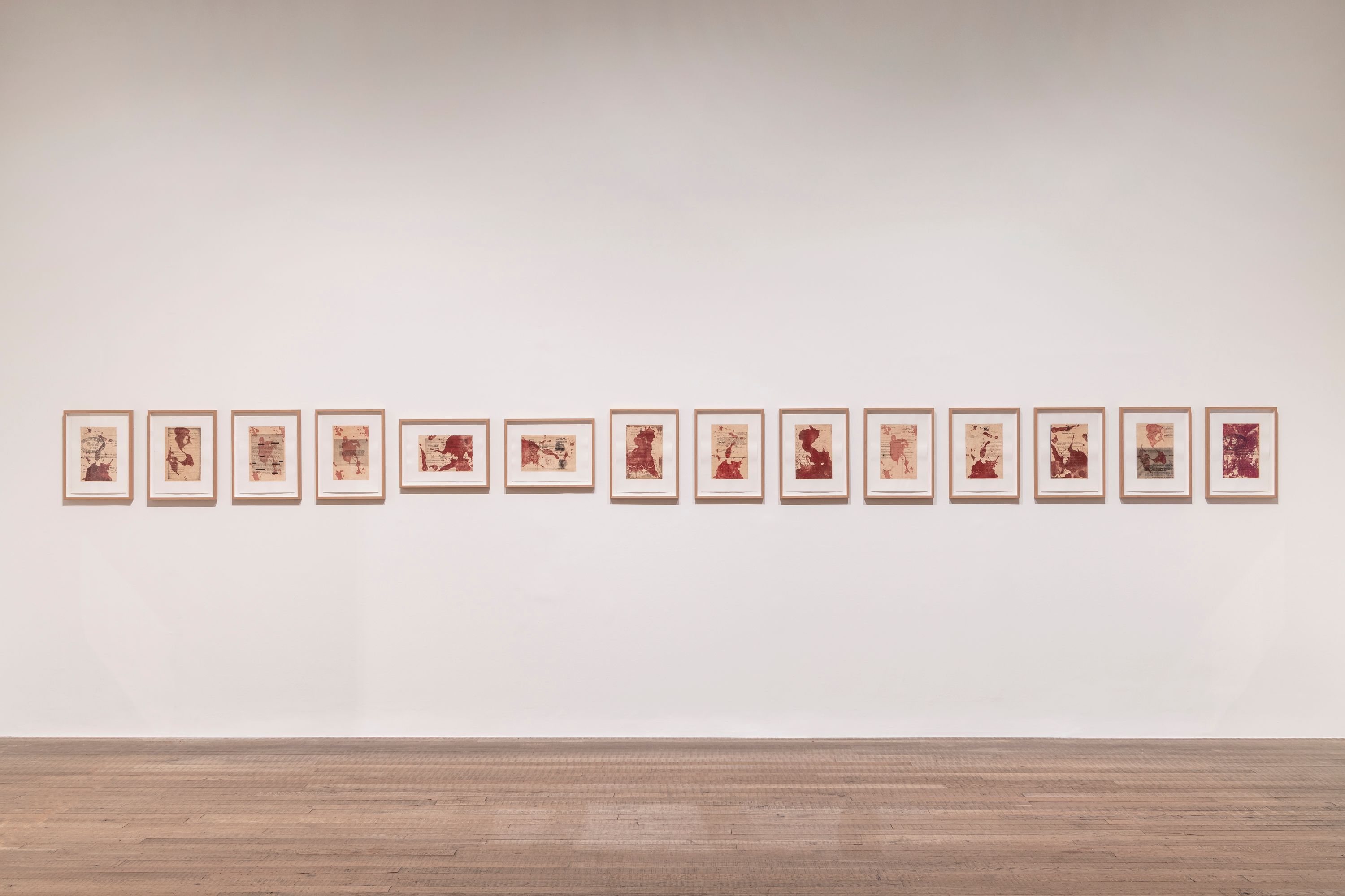 An art gallery featuring a wooden floor and bench with various pieces of artwork displayed on white walls.