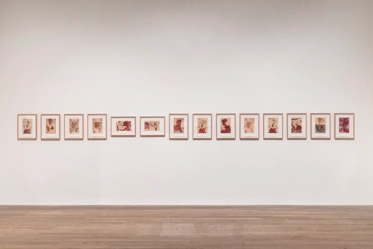 An art gallery featuring a wooden floor and bench with various pieces of artwork displayed on white walls.