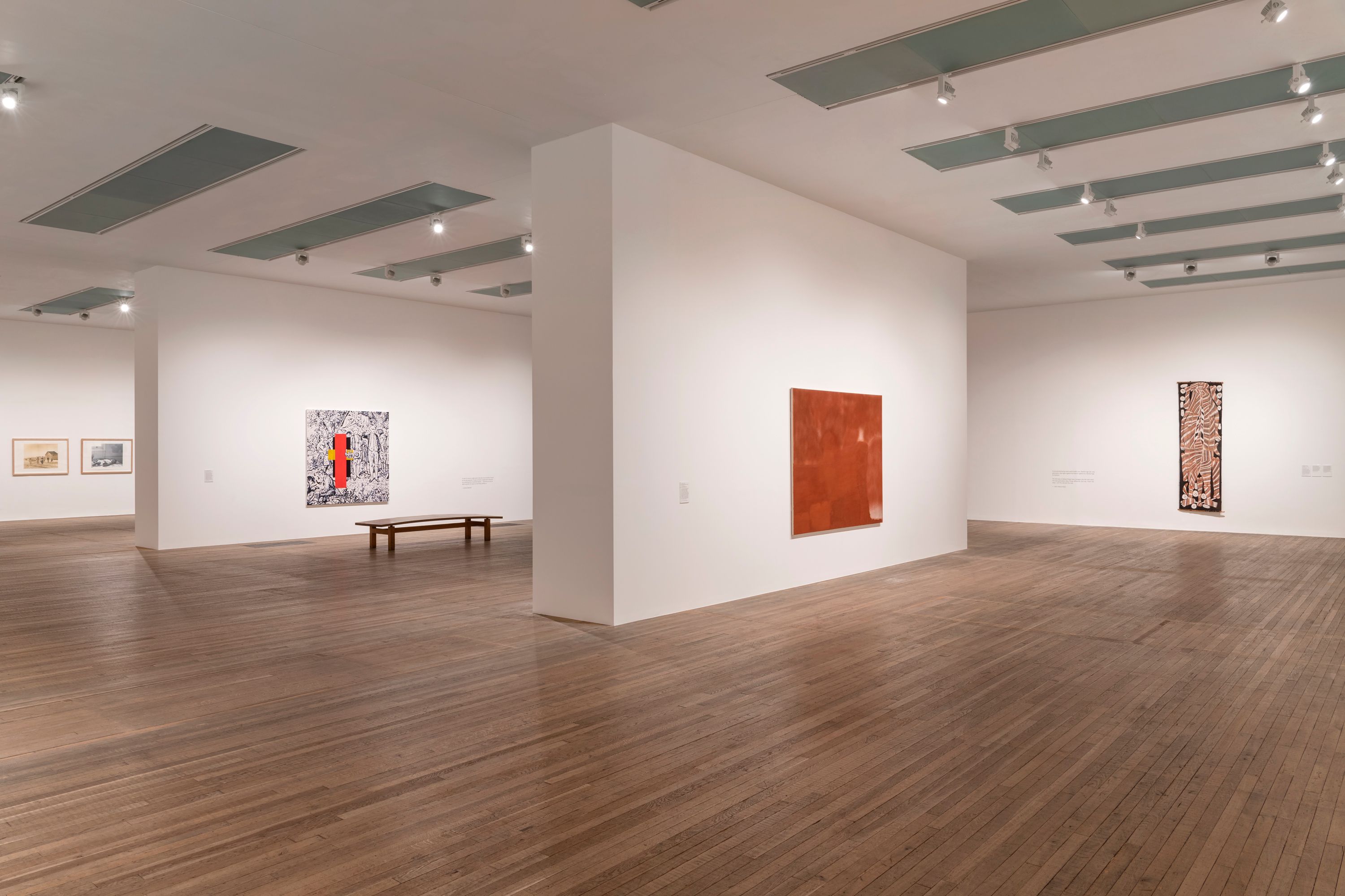 Spacious art gallery with white walls and wooden floors, displaying various artworks.