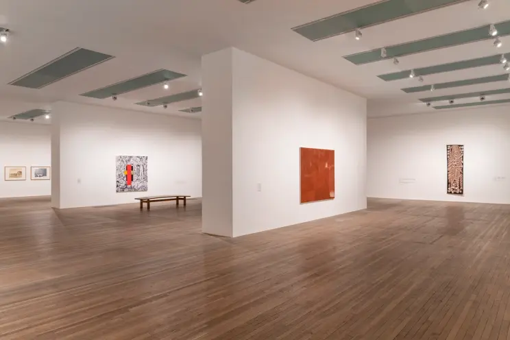 Spacious art gallery with white walls and wooden floors, displaying various artworks.