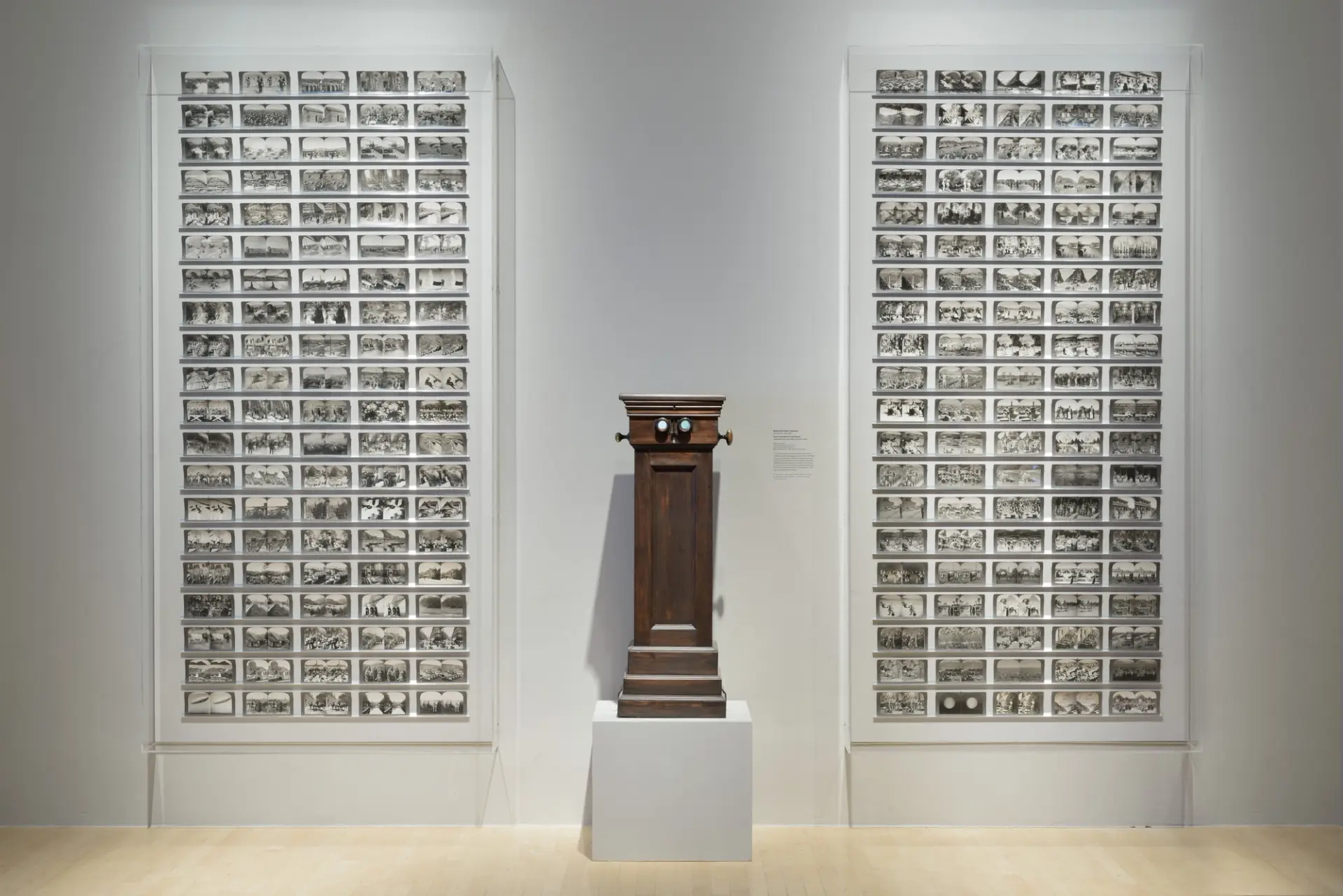 Two large frames filled with black and white photographs arranged in five columns hang on a white wall. Situated between t...