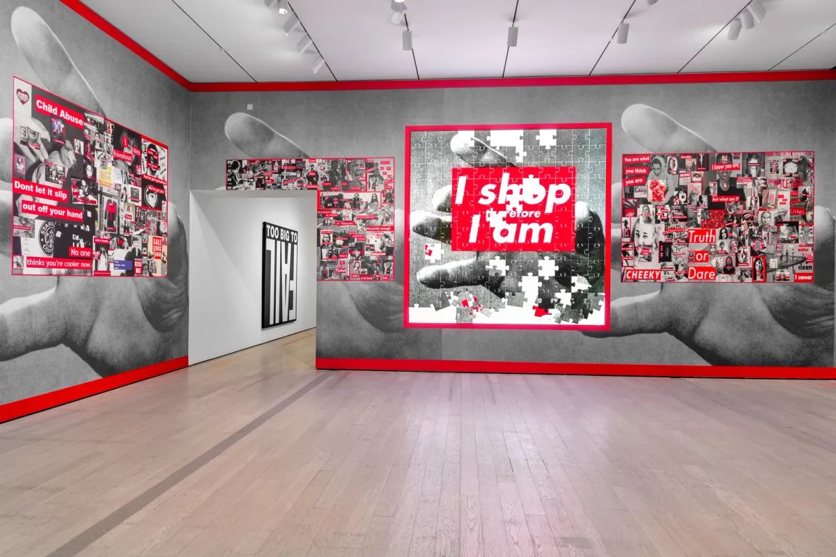 Black and white posters depicting hands grabbing, accompanied by red captions, displayed in a gallery room.