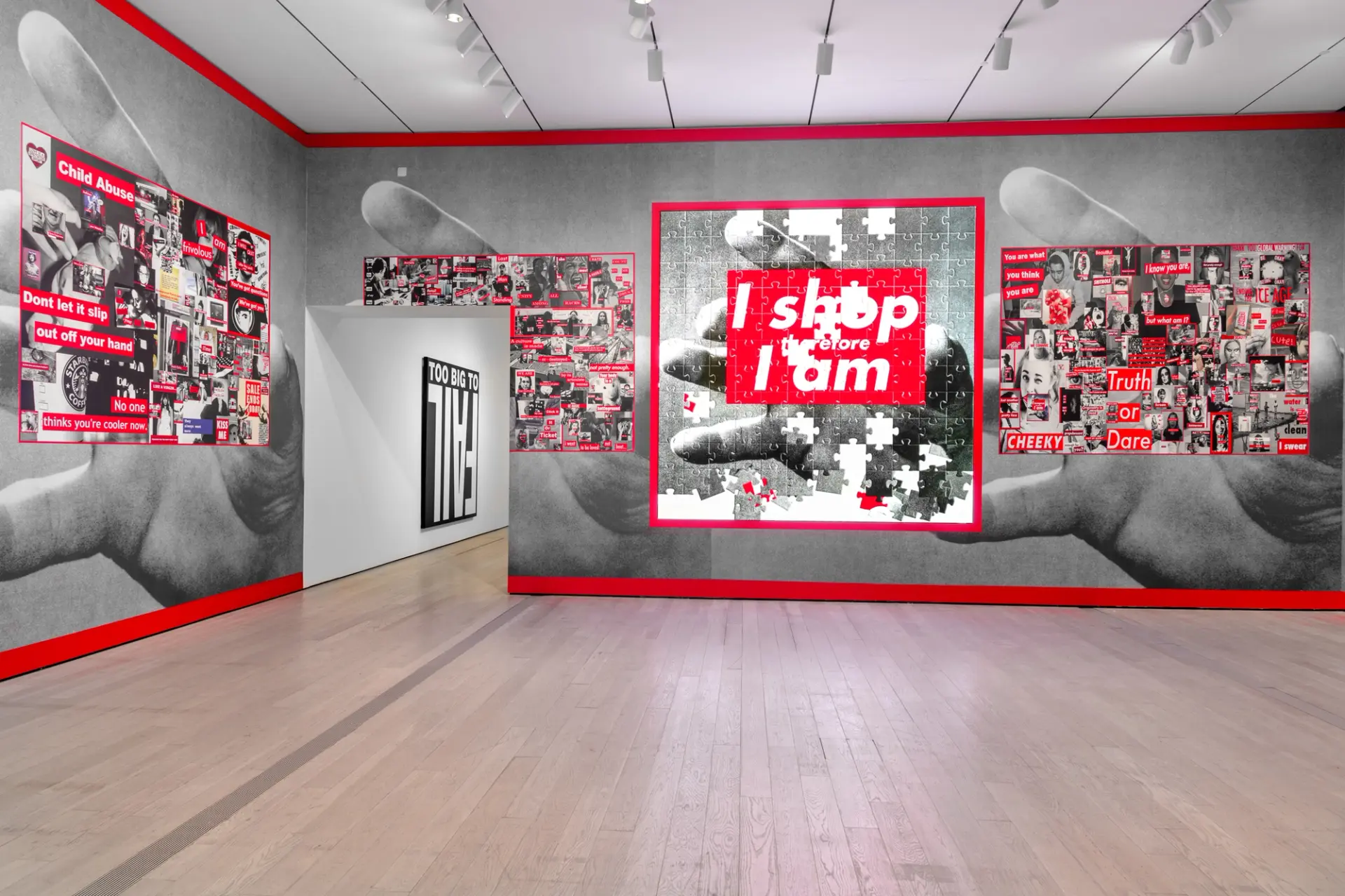 Black and white posters depicting hands grabbing, accompanied by red captions, displayed in a gallery room.