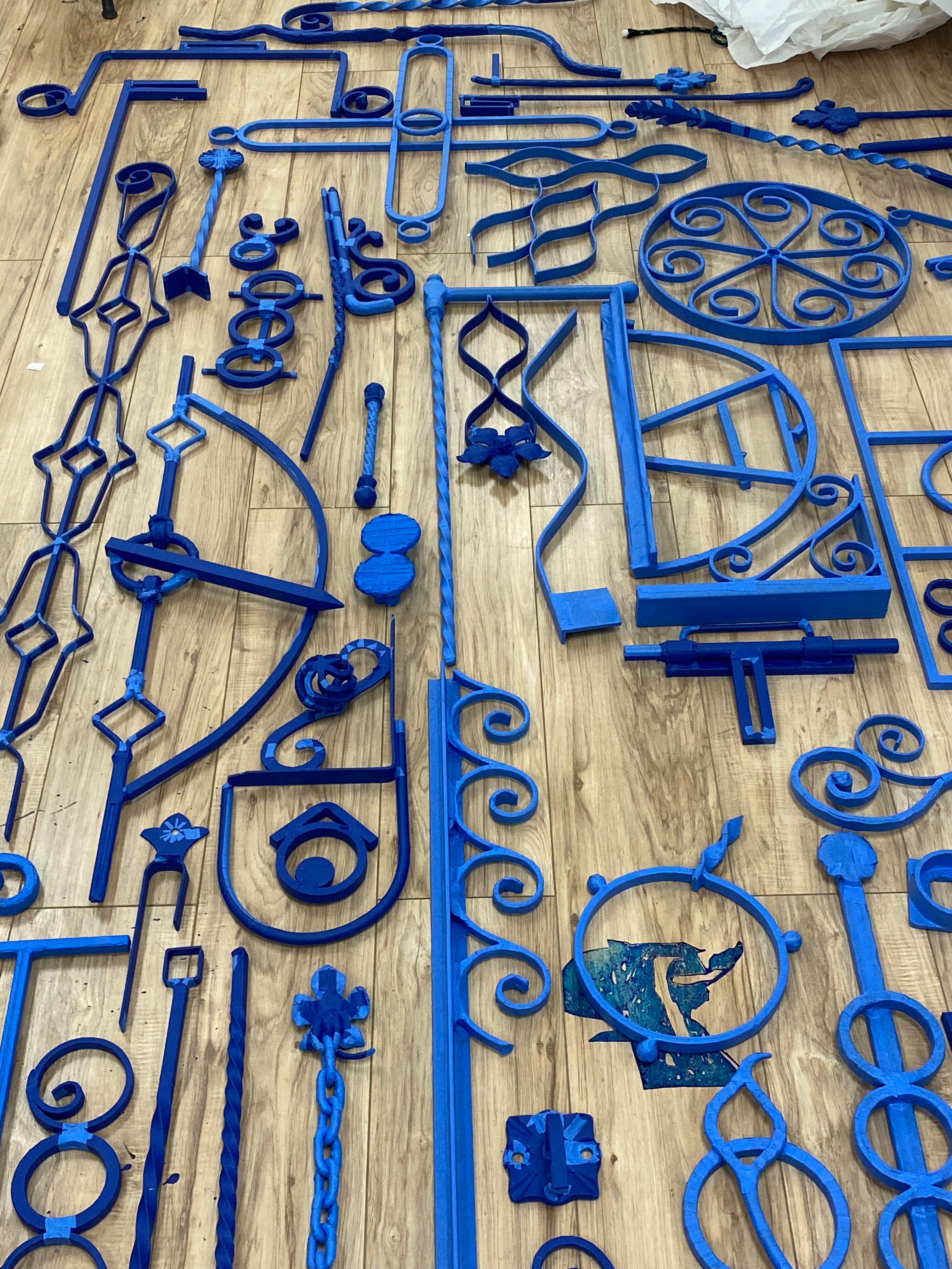 Vivid blue sculptural elements spread across a studio floor, showcasing a variety of shapes and symbols in a dynamic arrangement.
