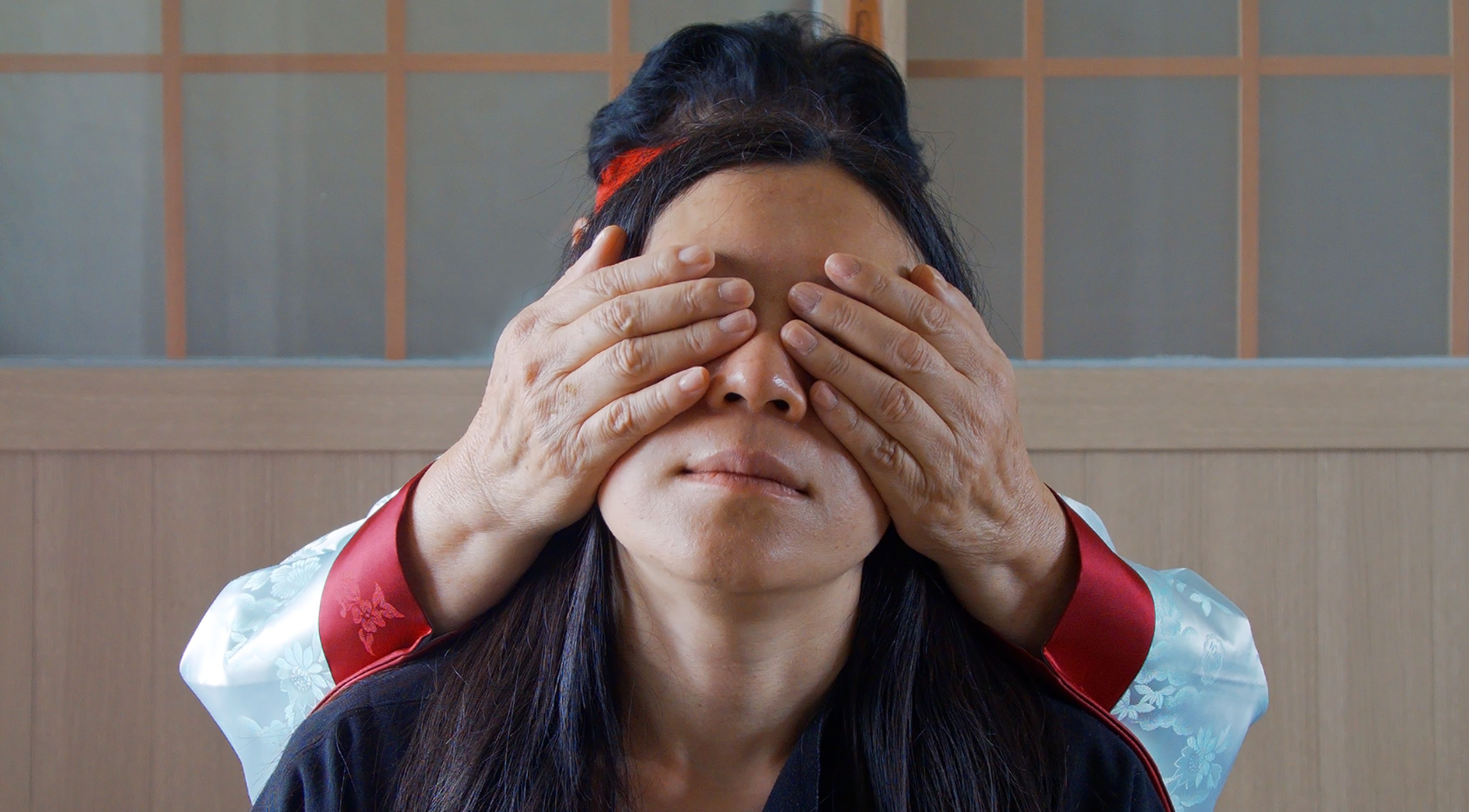 A person stands in a still shot from the projected film "Community of Parting", 2019. Another person behind them covers th...