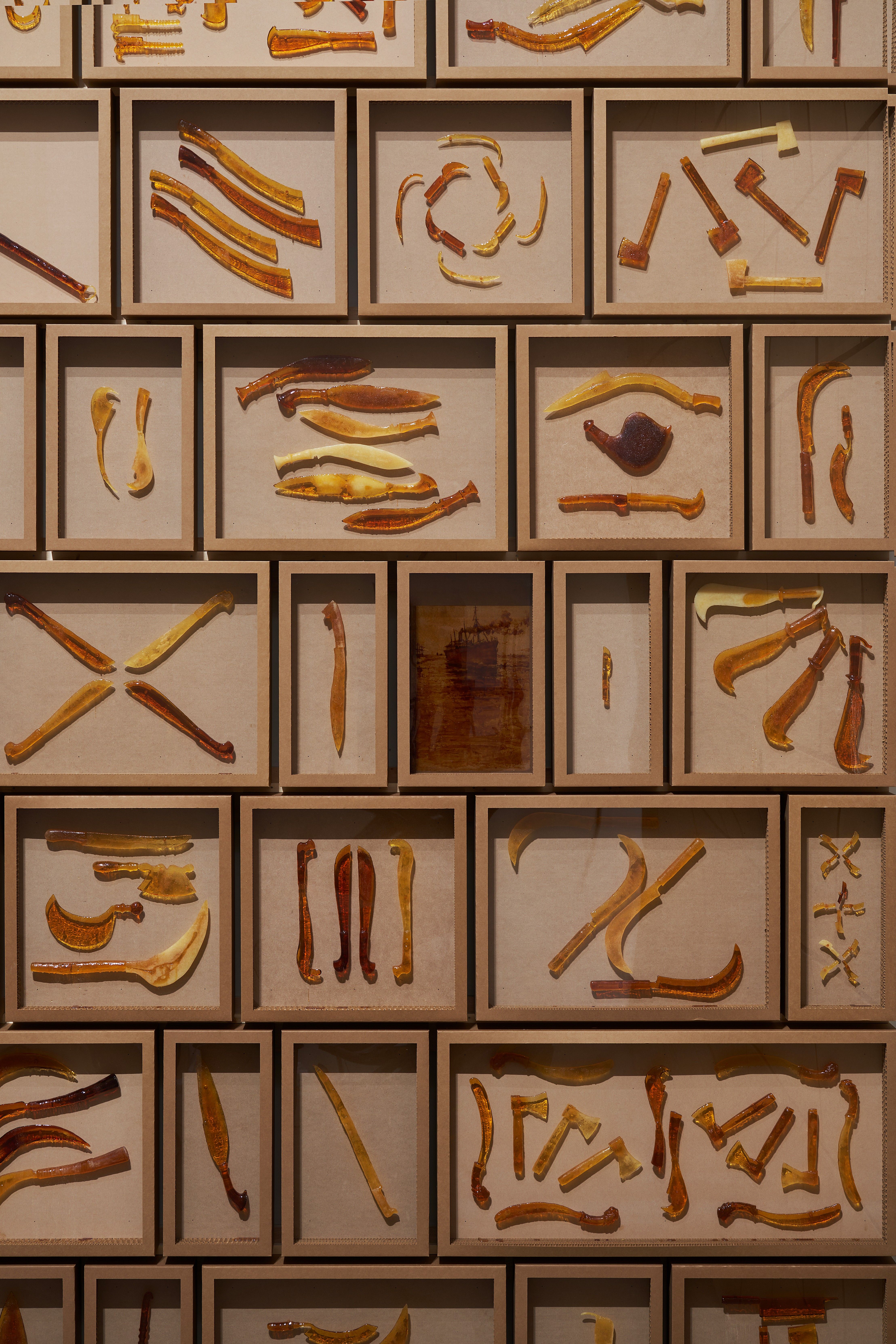 Close-up of a wall filled with individual boxes showcasing a variety of amber-hued wood carvings.