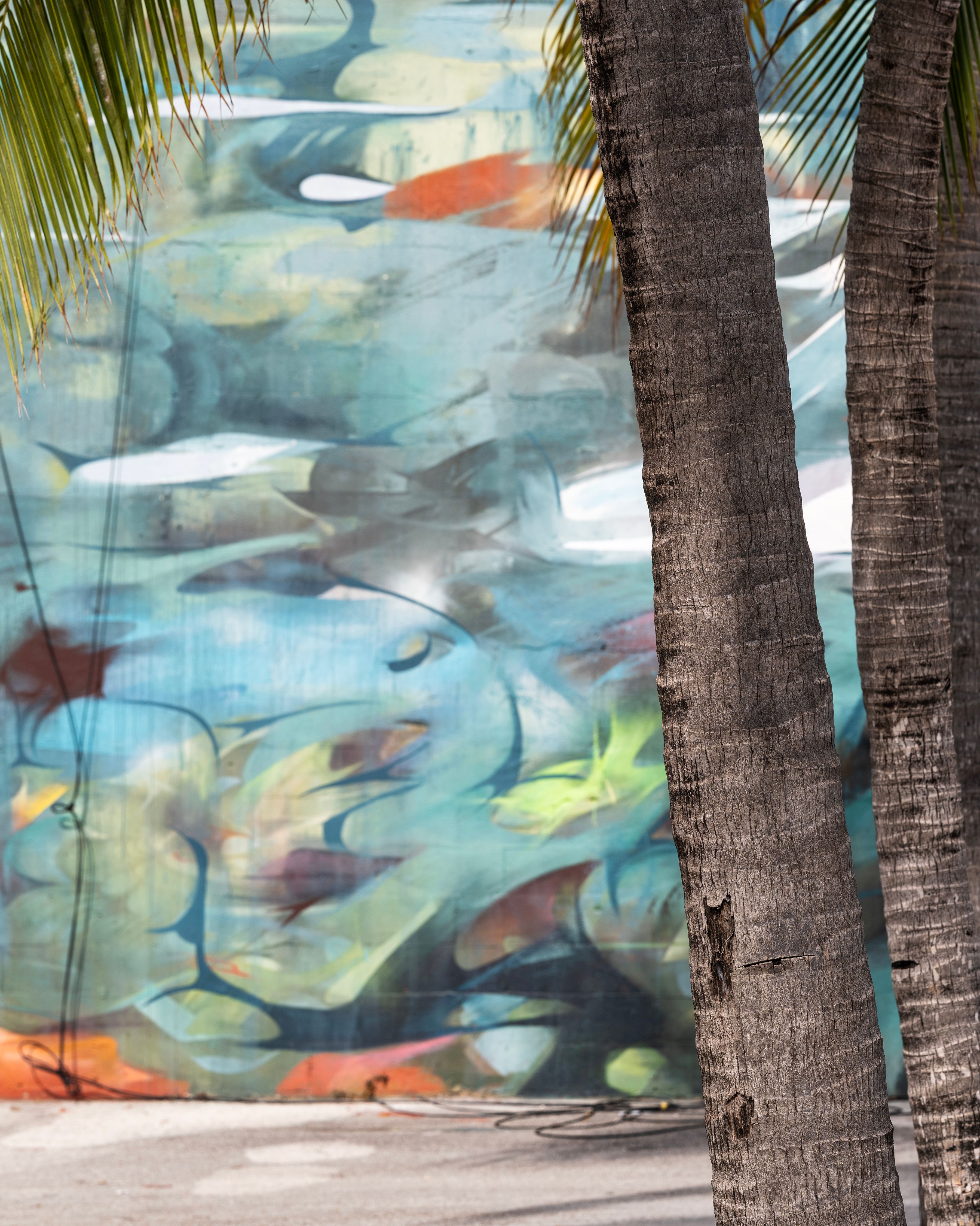 Abstract mural with blue and green hues obscured by palm trees in foreground.