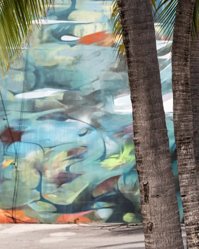 Abstract mural with blue and green hues obscured by palm trees in foreground.