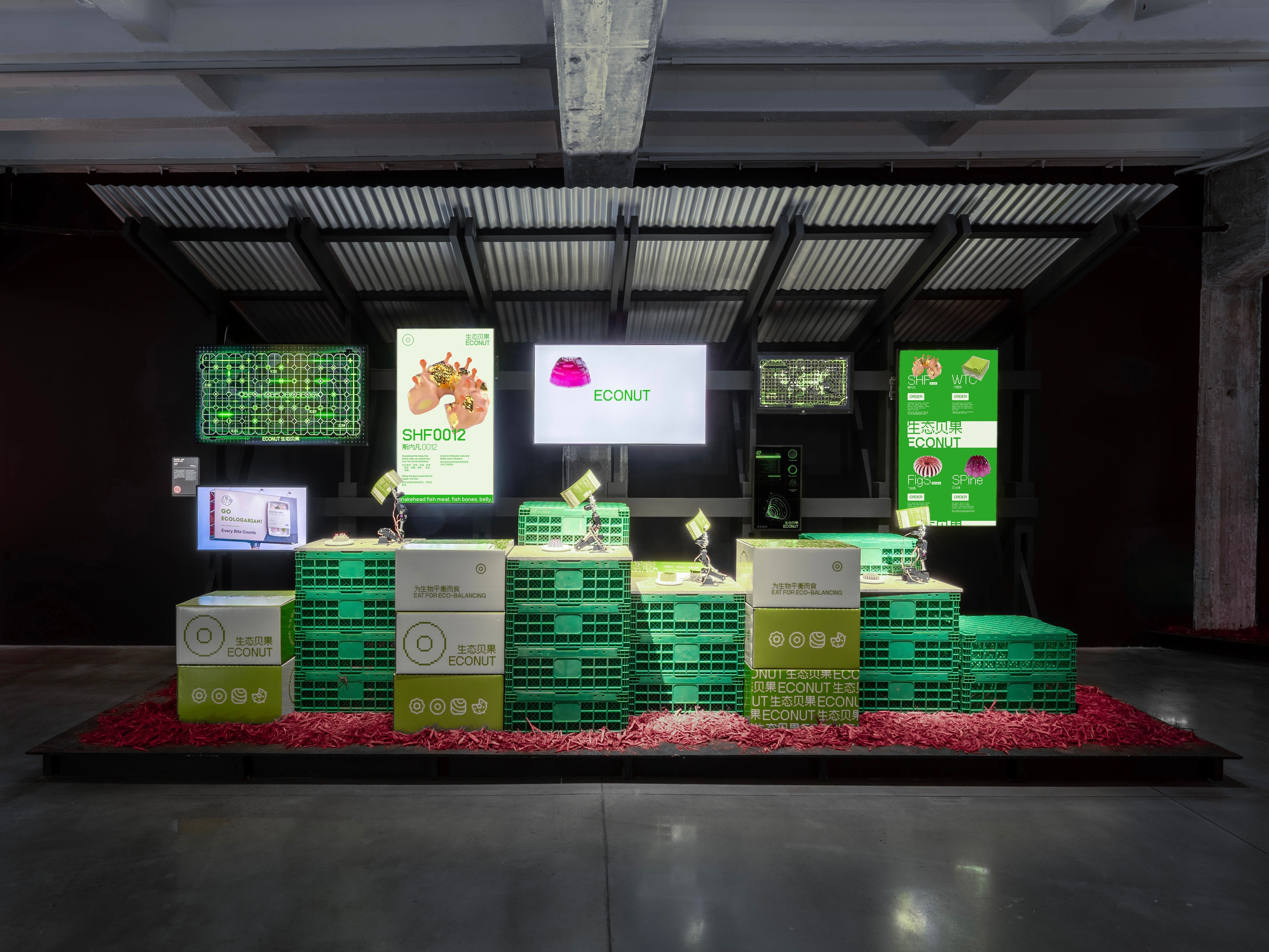 Exhibition installation with stacked green crates, screens displaying "ECONUT" and other graphics.