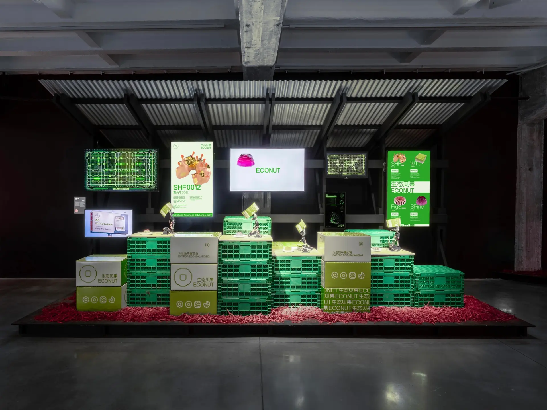 Exhibition installation with stacked green crates, screens displaying "ECONUT" and other graphics.